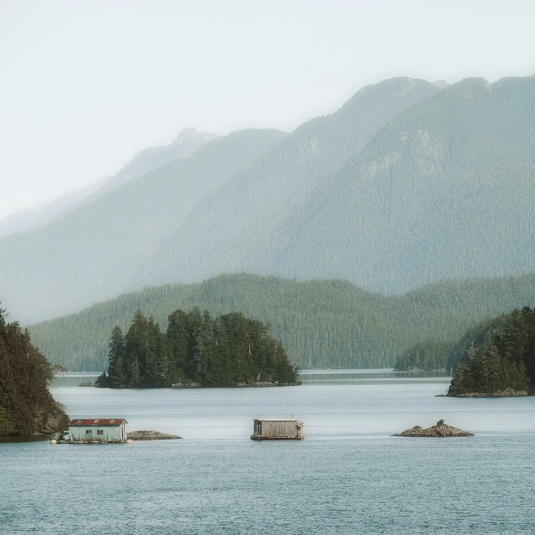 A serene lake with small islands, surrounded by forested hills and mountains in the background, with a misty atmosphere.
