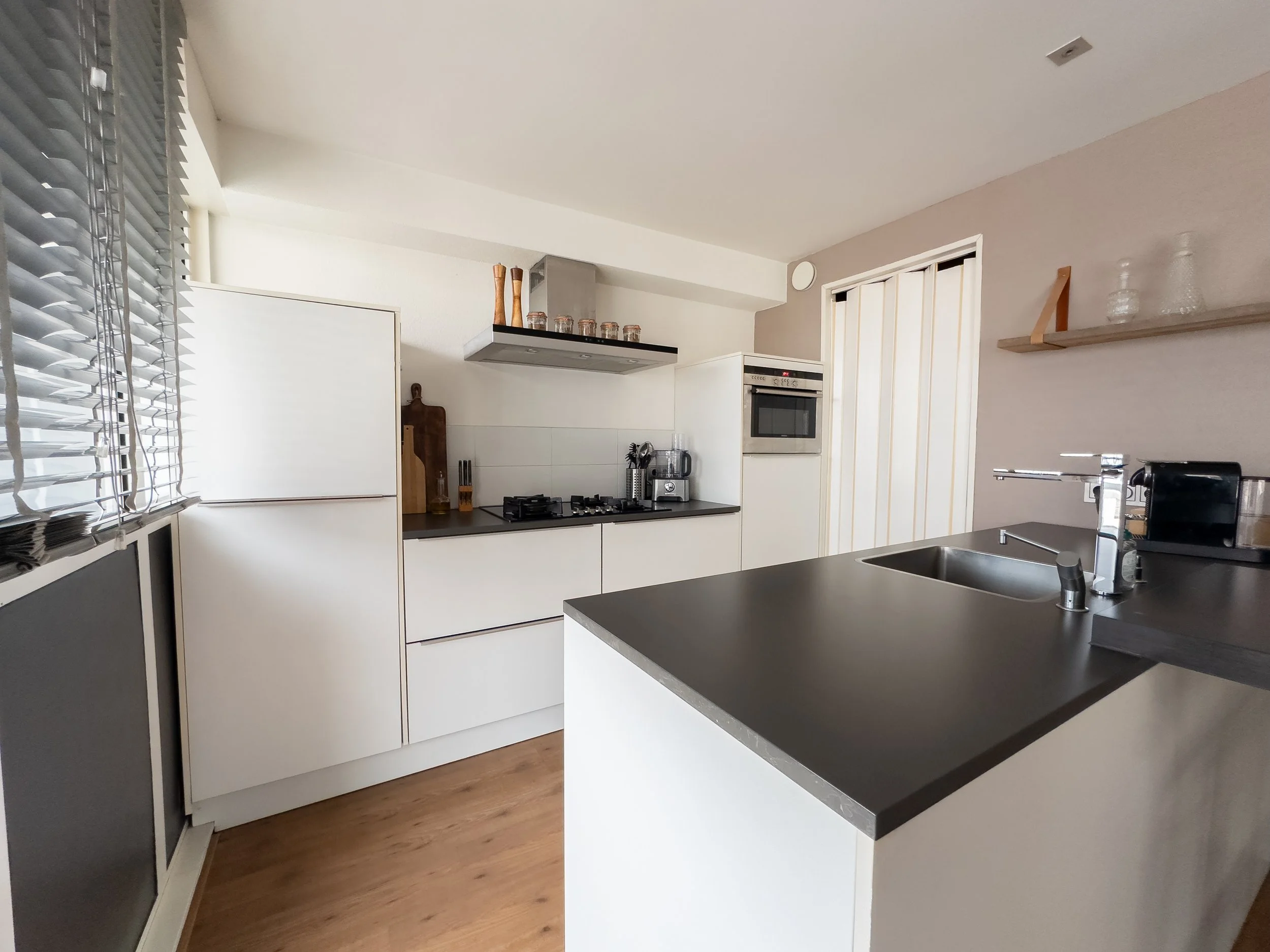 Modern kitchen with white cabinets, black countertops, a stainless steel sink, and appliances including a gas stove, oven, microwave, and coffee maker.