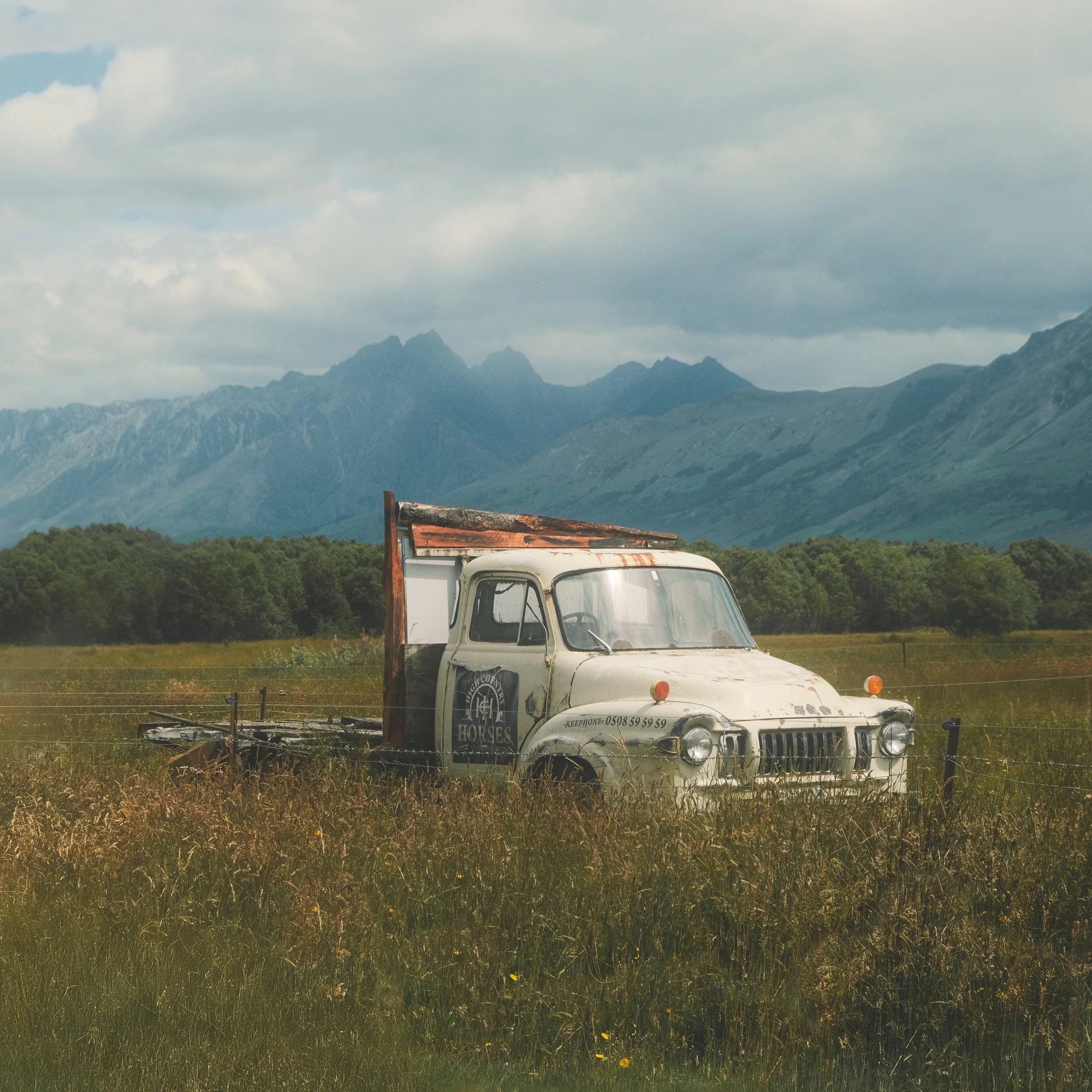 An old, abandoned truck in a grassy field with mountains and cloudy sky in the background. New Zealand landscape photogtraphy