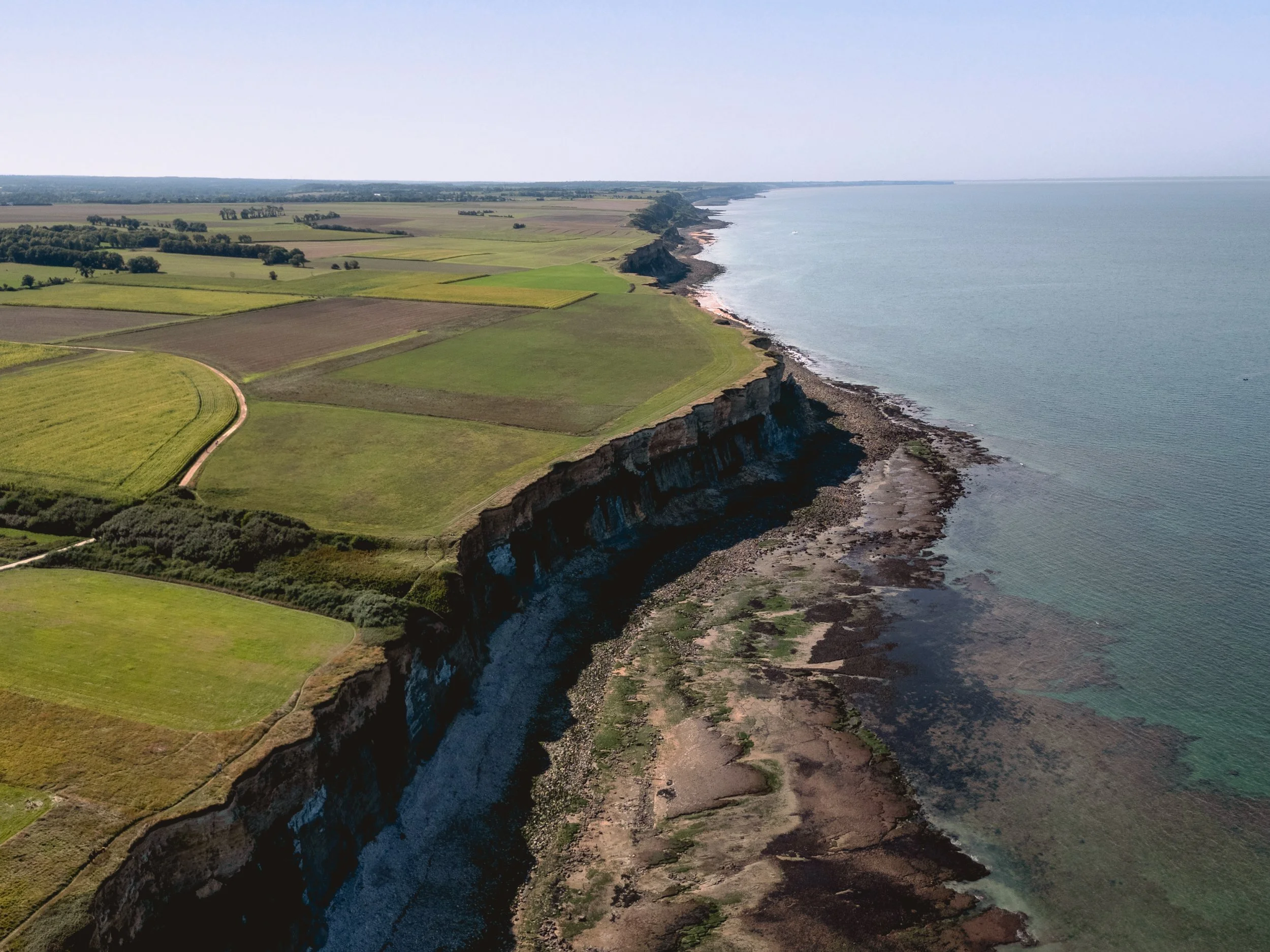 Aerial view of green farmland and a rugged coastline with white cliffs meeting the ocean.