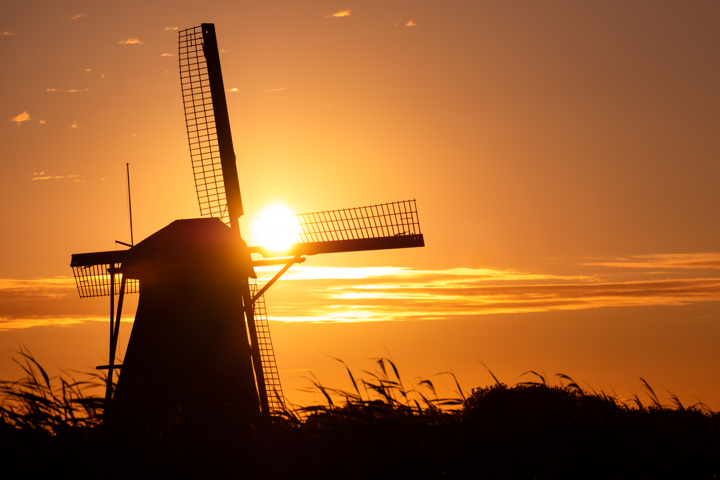 Silhouette of a windmill against a sunset sky with orange and yellow hues.