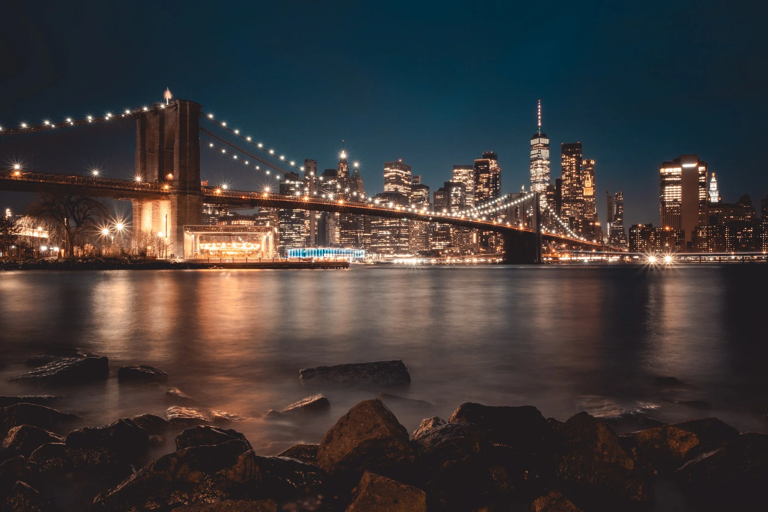 Night view of the Brooklyn Bridge and Manhattan skyline reflected on water with city lights