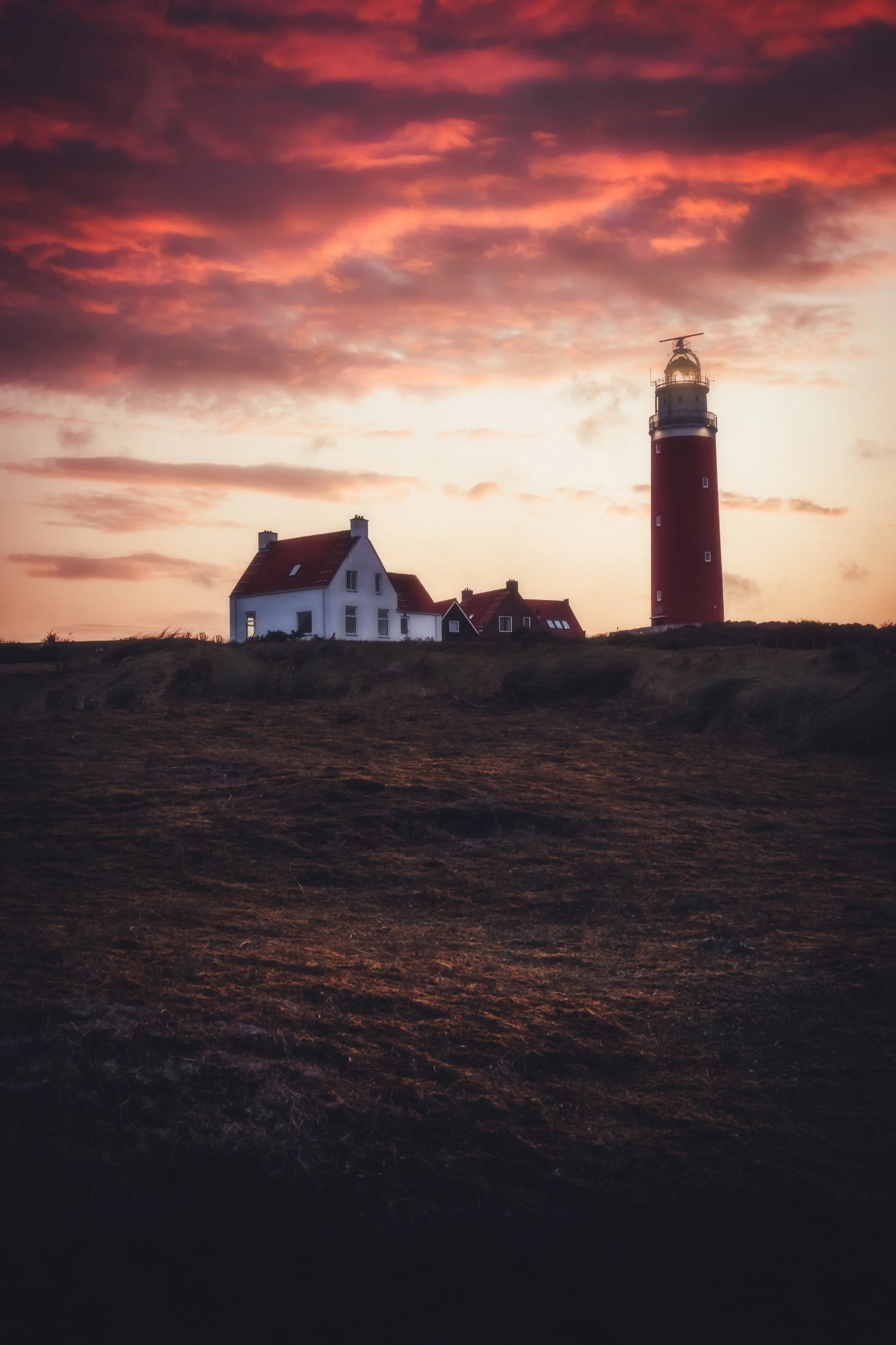 Sunset over a lighthouse and houses on a hill.