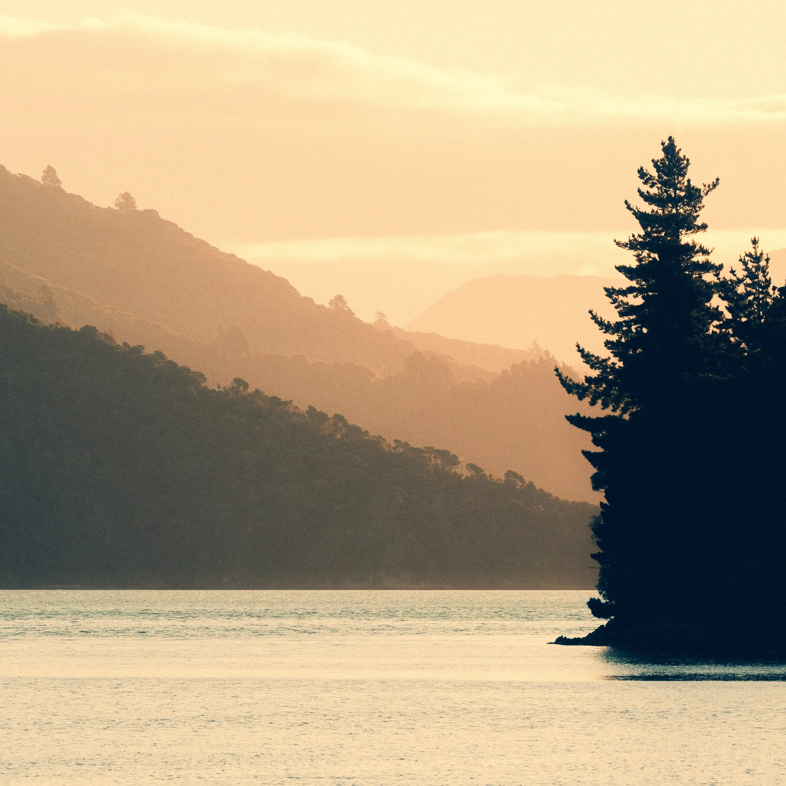 Sunset over a body of water with mountains and trees in the background