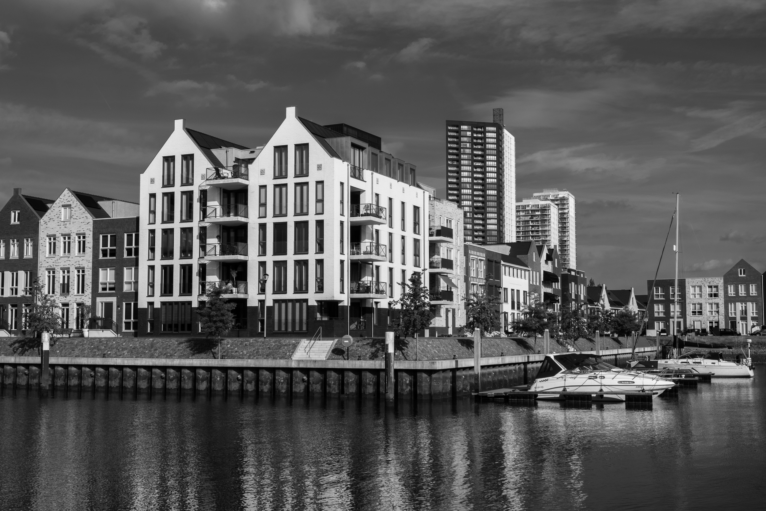 A black and white photo of modern waterfront buildings with boats docked in the water.
