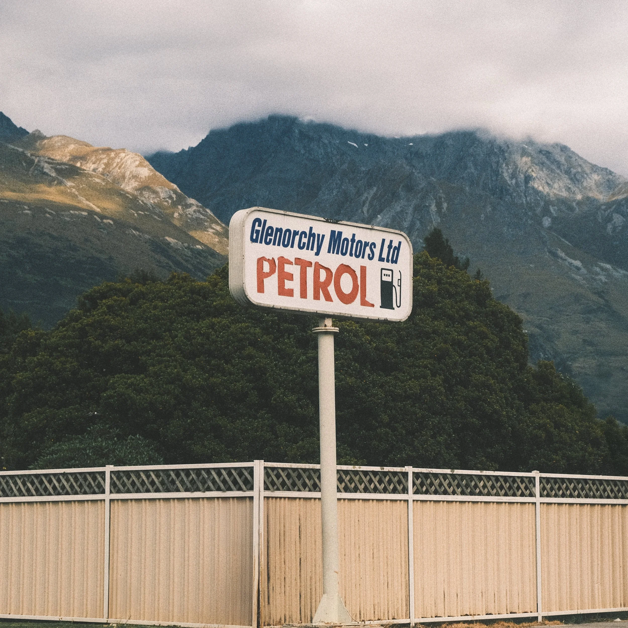A sign for Glenorchy Motors Ltd advertising petrol, with a mountain and cloudy sky in the background.