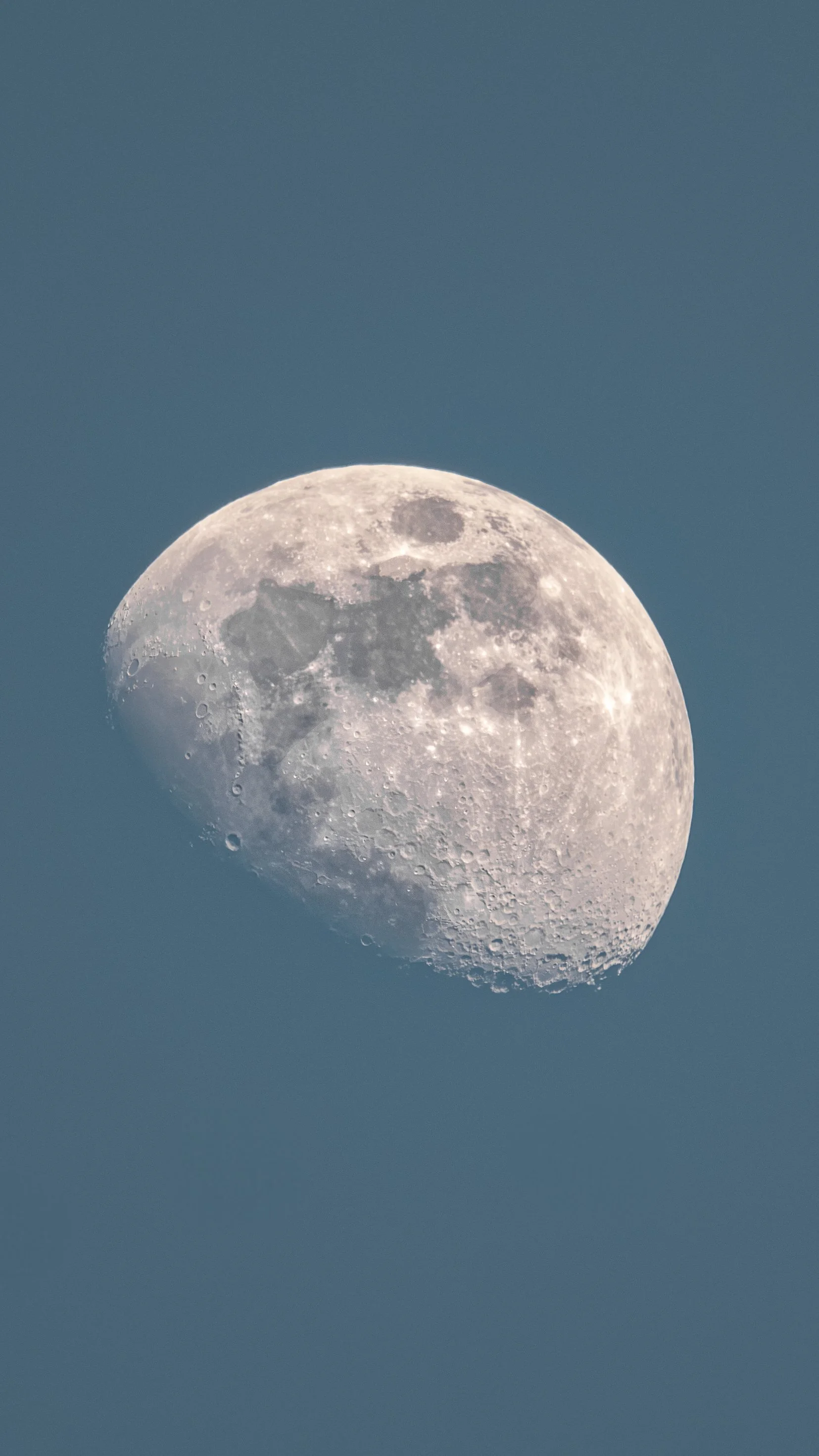 Close-up image of the moon in a waxing gibbous phase, with visible craters and surface details, against a clear blue sky.