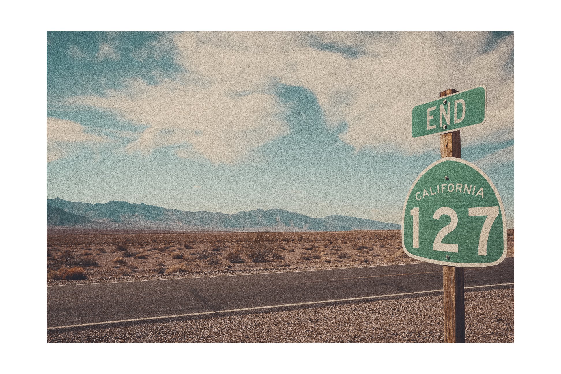 A desert landscape with mountains in the background, a road in the foreground, and road signs indicating the end of California State Route 127.