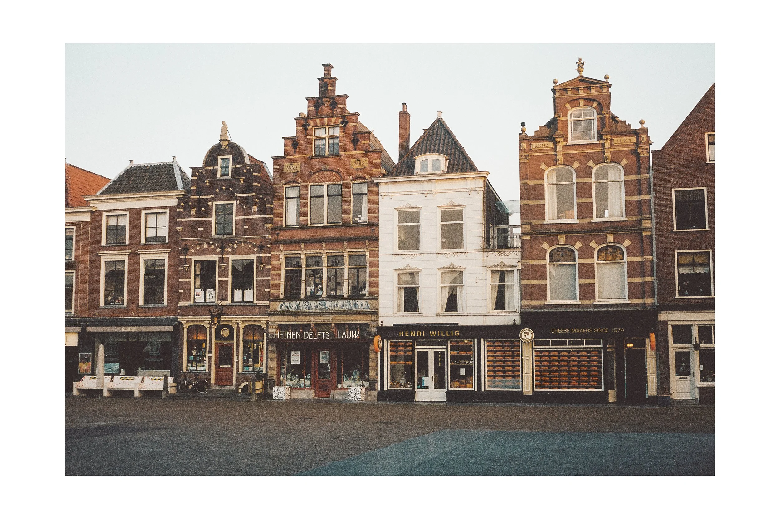 Three-story historic buildings with storefronts on the ground level in a European city street during daytime.