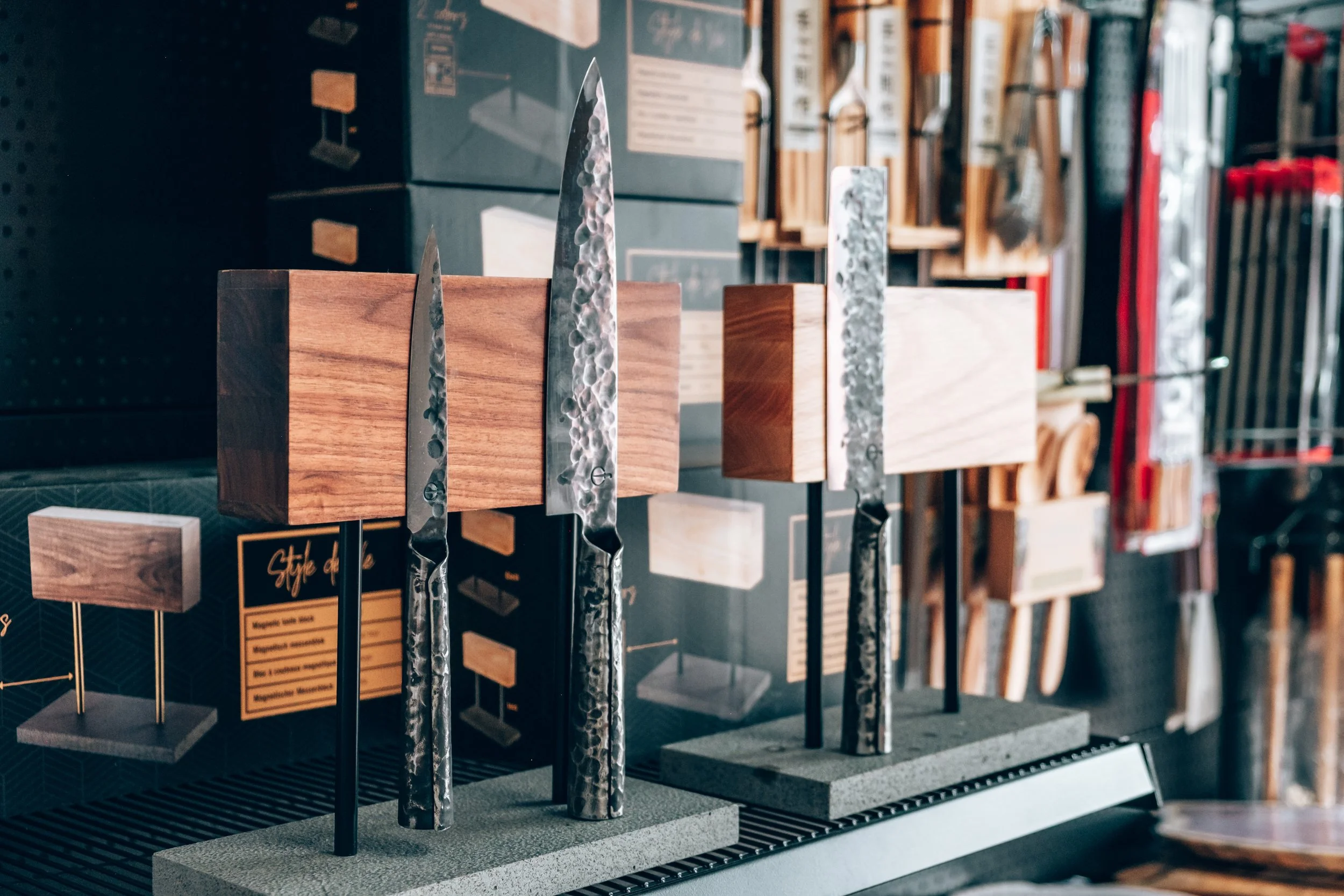 Display of handcrafted knives with hammered metal blades mounted on wooden blocks in a store.