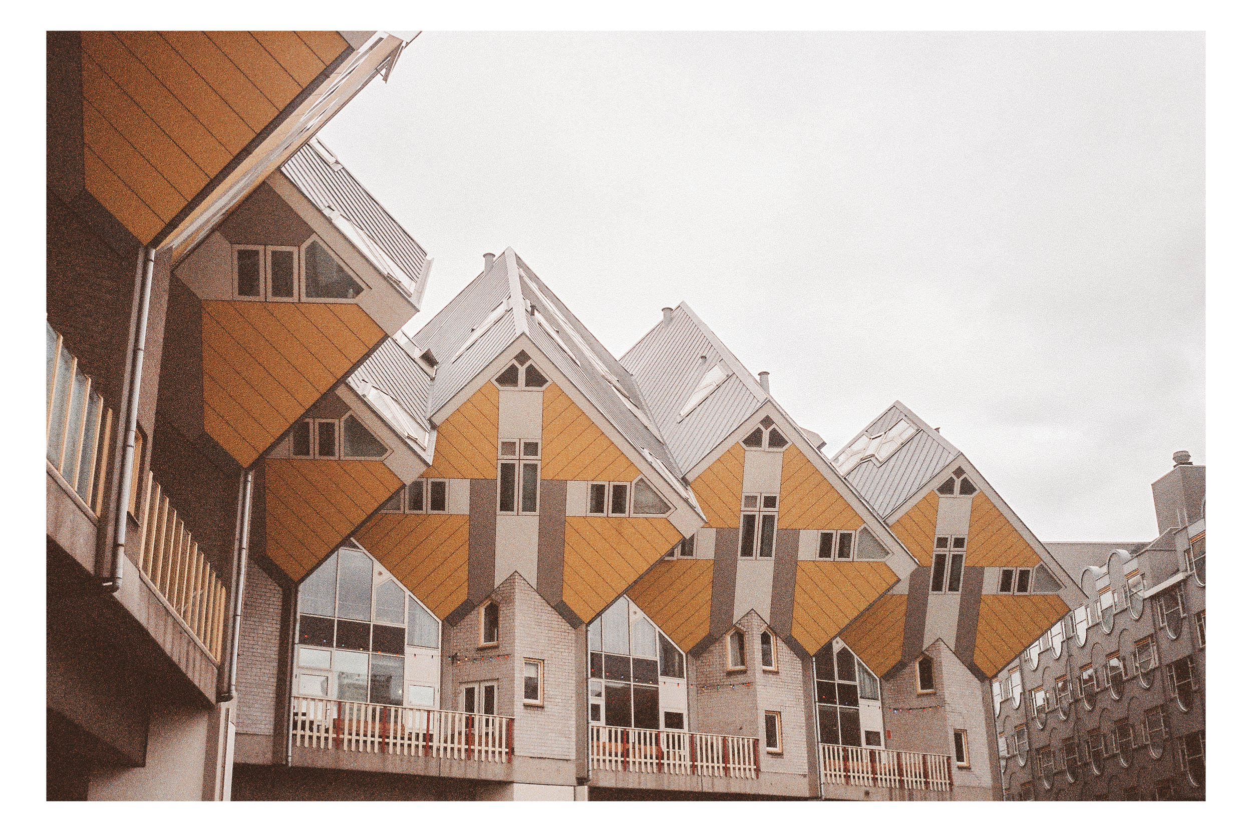 A modern residential building with unique angular yellow and white roofs, multiple windows, and balconies, set against a cloudy sky.