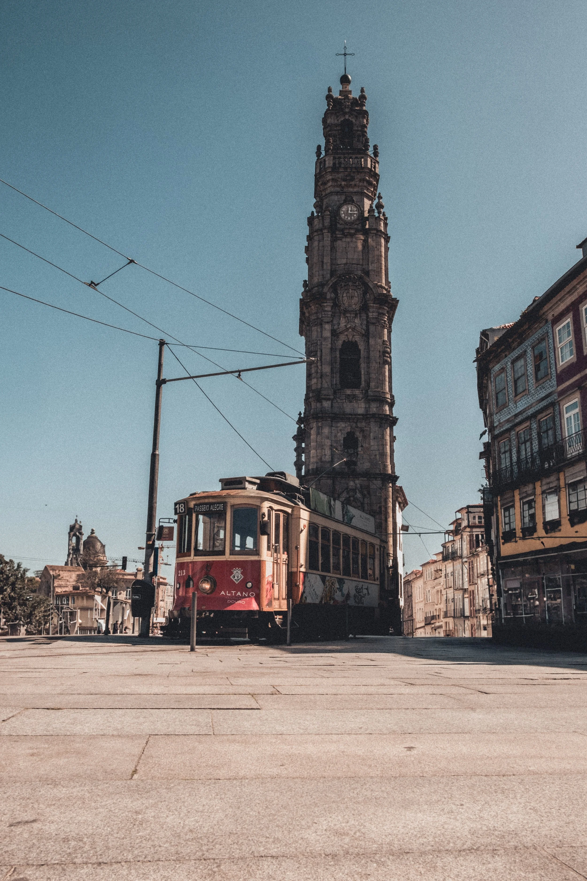 Historical tower with a clock, tram in front, and old buildings on the street under a clear blue sky in an urban setting. Porto Portugal landscape photogtraphy
