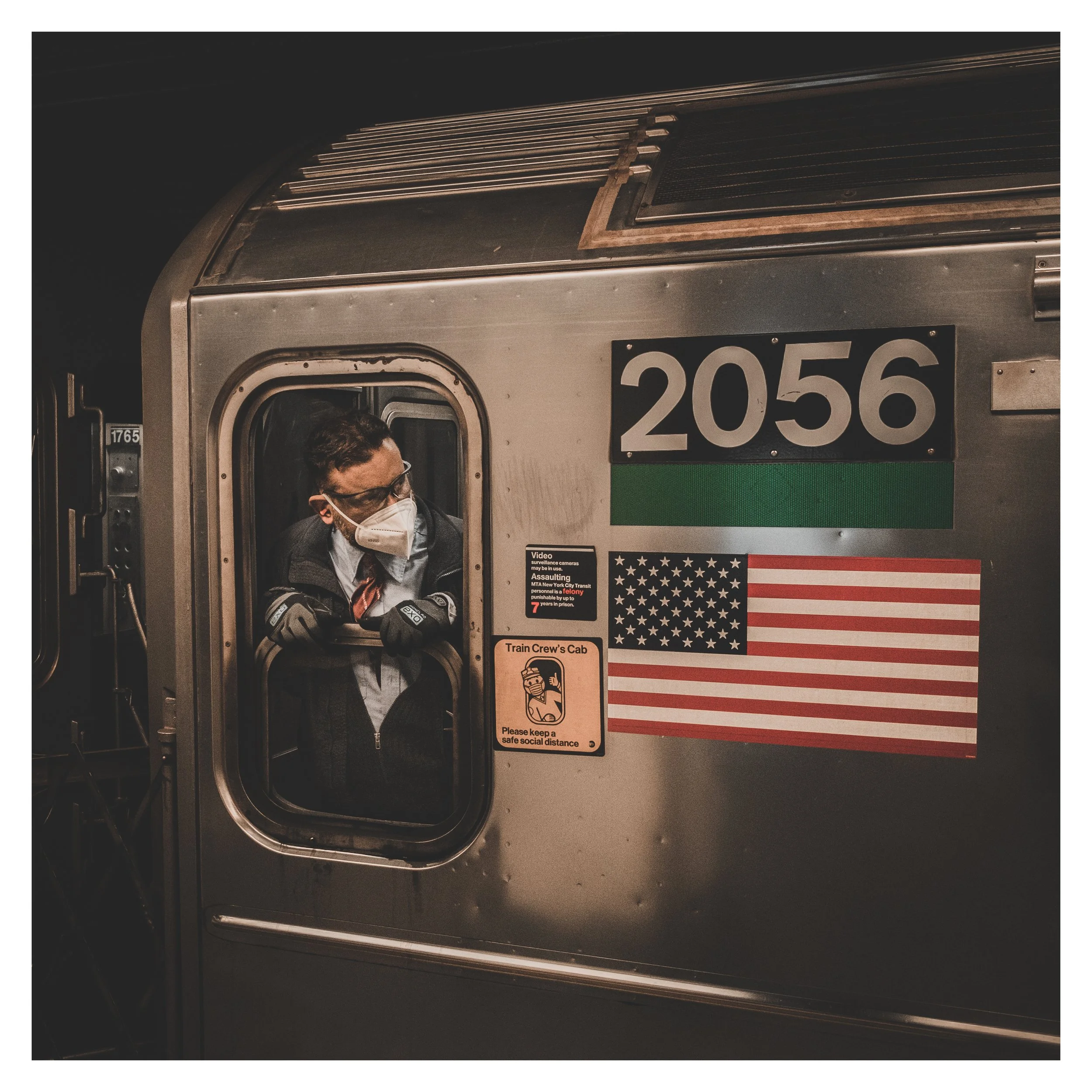 A man wearing glasses, a mask, and a jacket looks out of a train door window. NEW YORK CITY SUBWAY