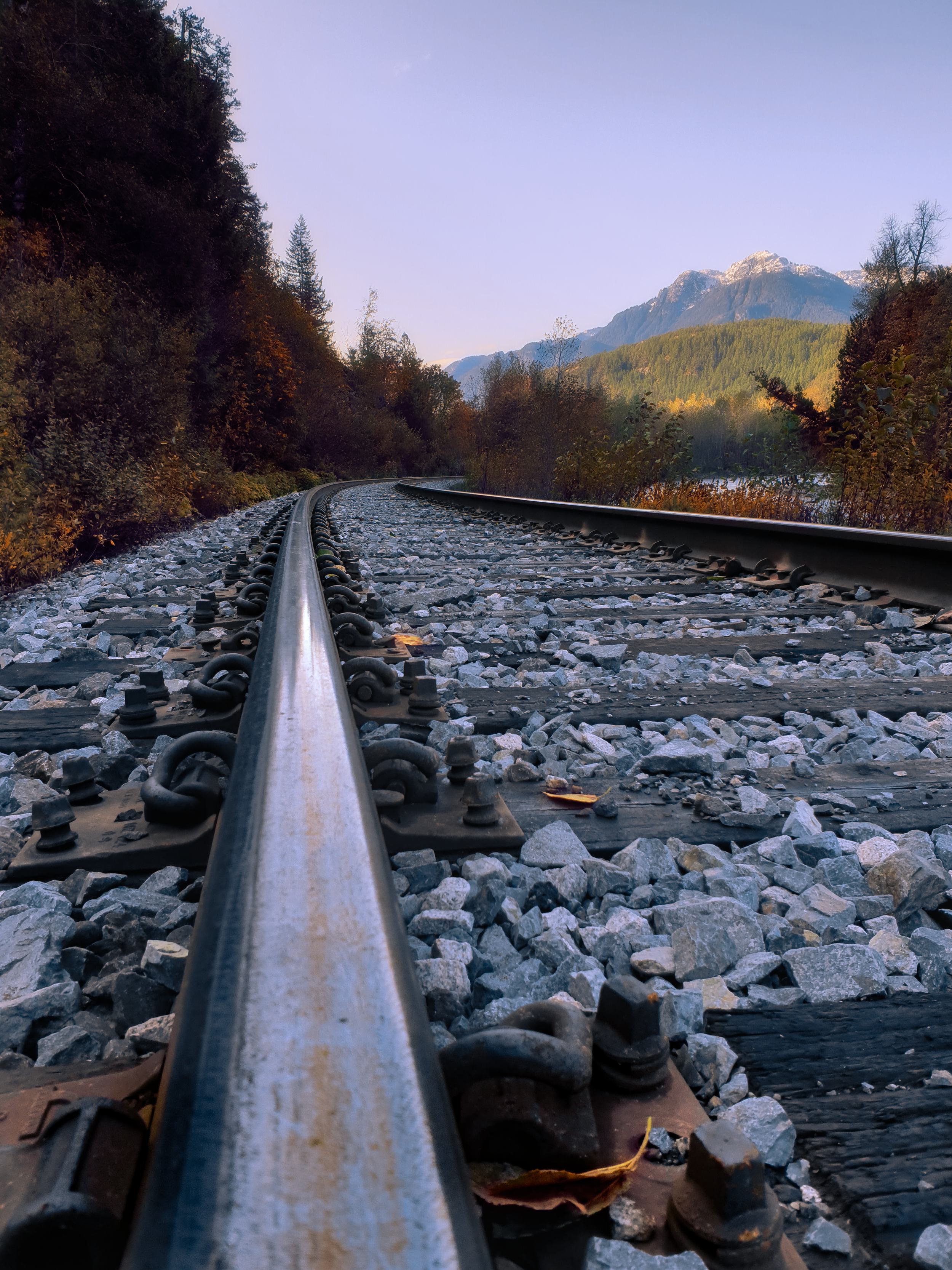 Close-up view of a railway track in a scenic mountainous landscape with trees and snow-capped mountains in the distance. Canada Landscape photography