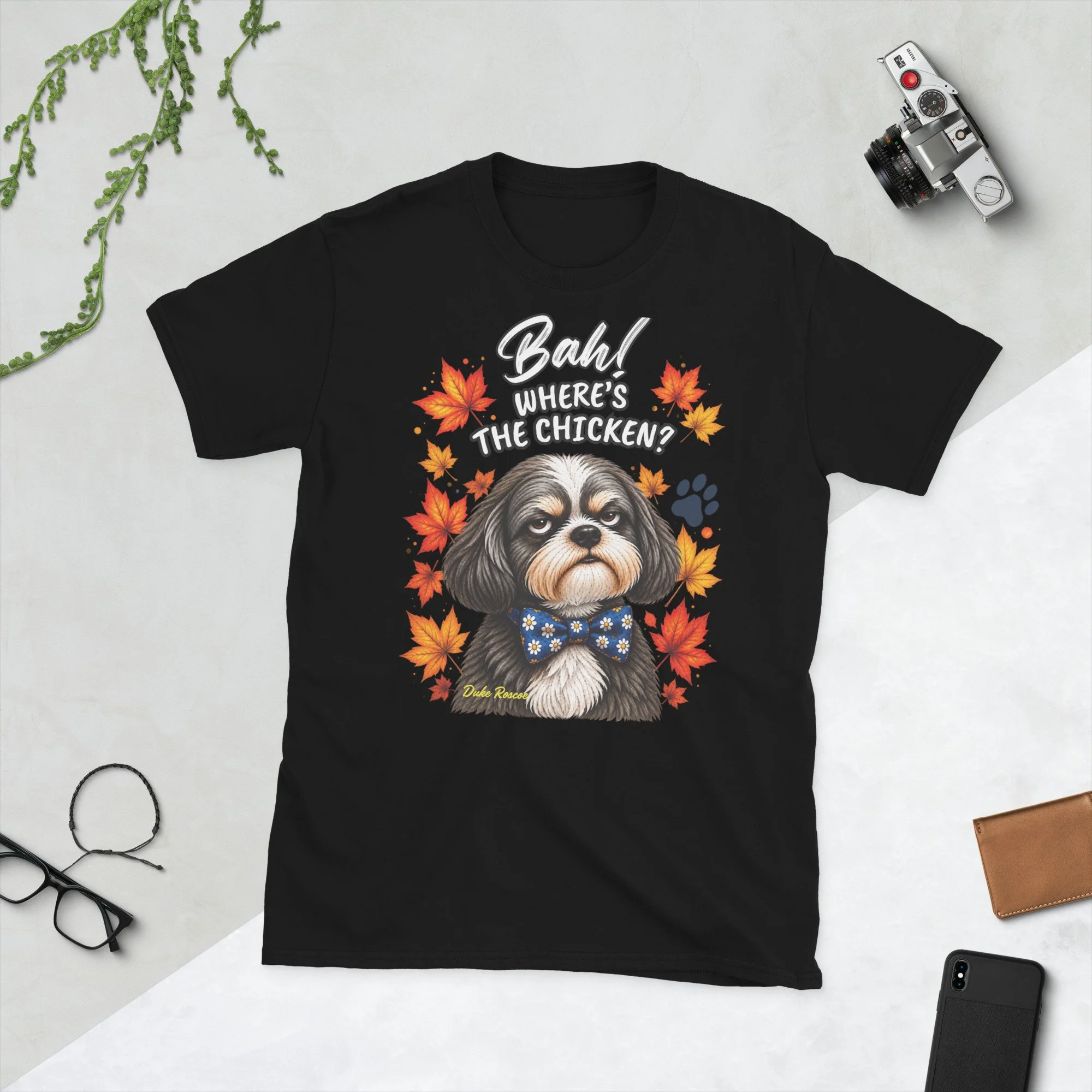 Bah! Where's the Chicken? Duke Roscoe Tee in black, flat lay: grumpy Shih Tzu in a blue bow tie amid autumn leaves