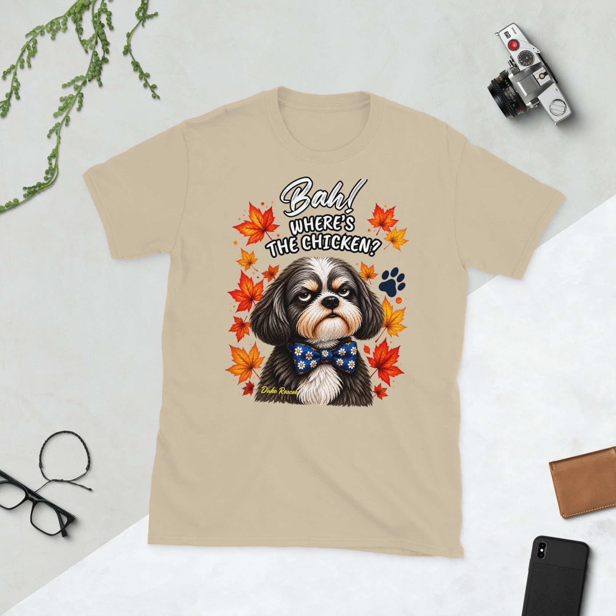 Bah! Where's the Chicken? Duke Roscoe Tee in sand, flat lay: grumpy Shih Tzu in a blue bow tie amid autumn leaves