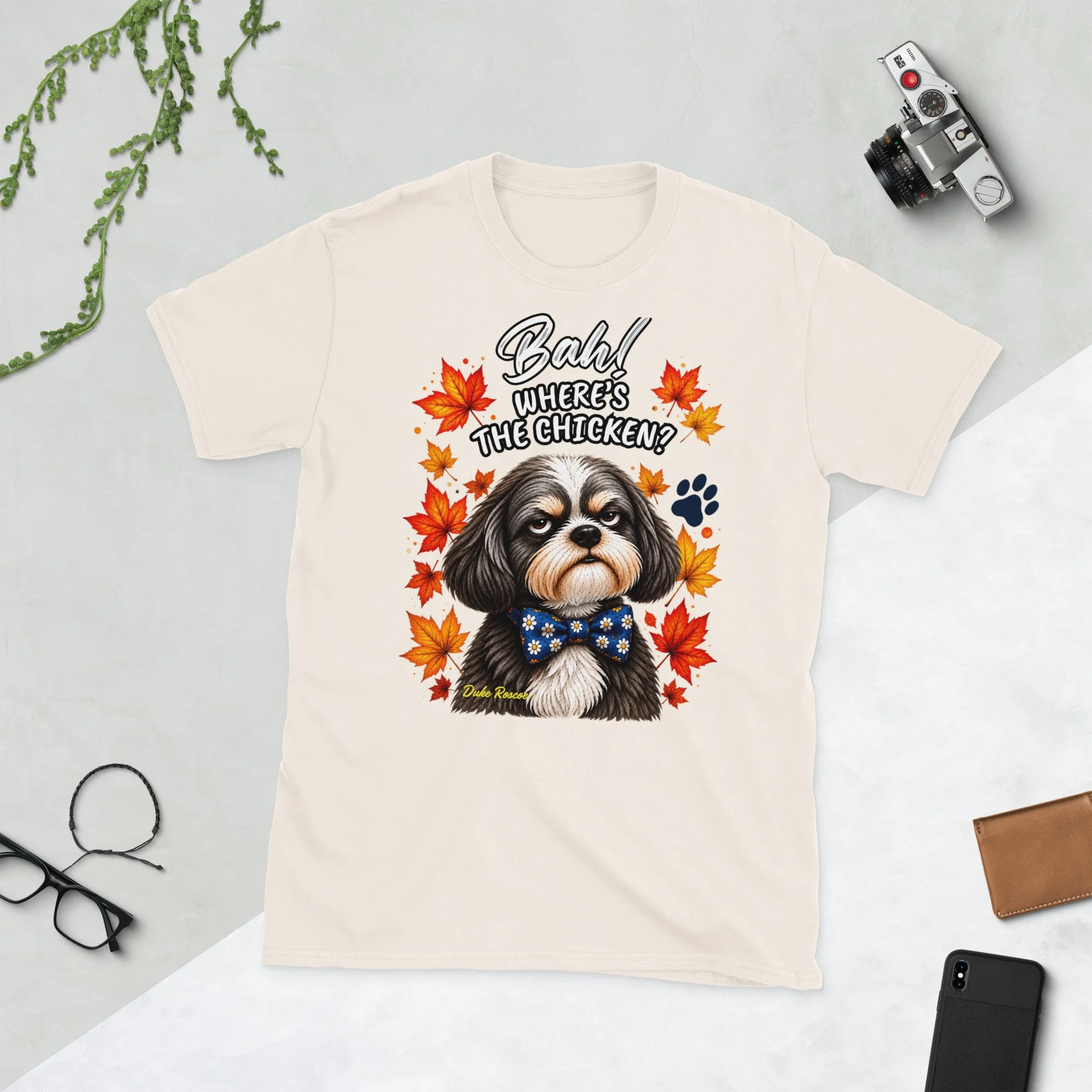 Bah! Where's the Chicken? Duke Roscoe Tee in natural, flat lay: grumpy Shih Tzu in a blue bow tie amid autumn leaves