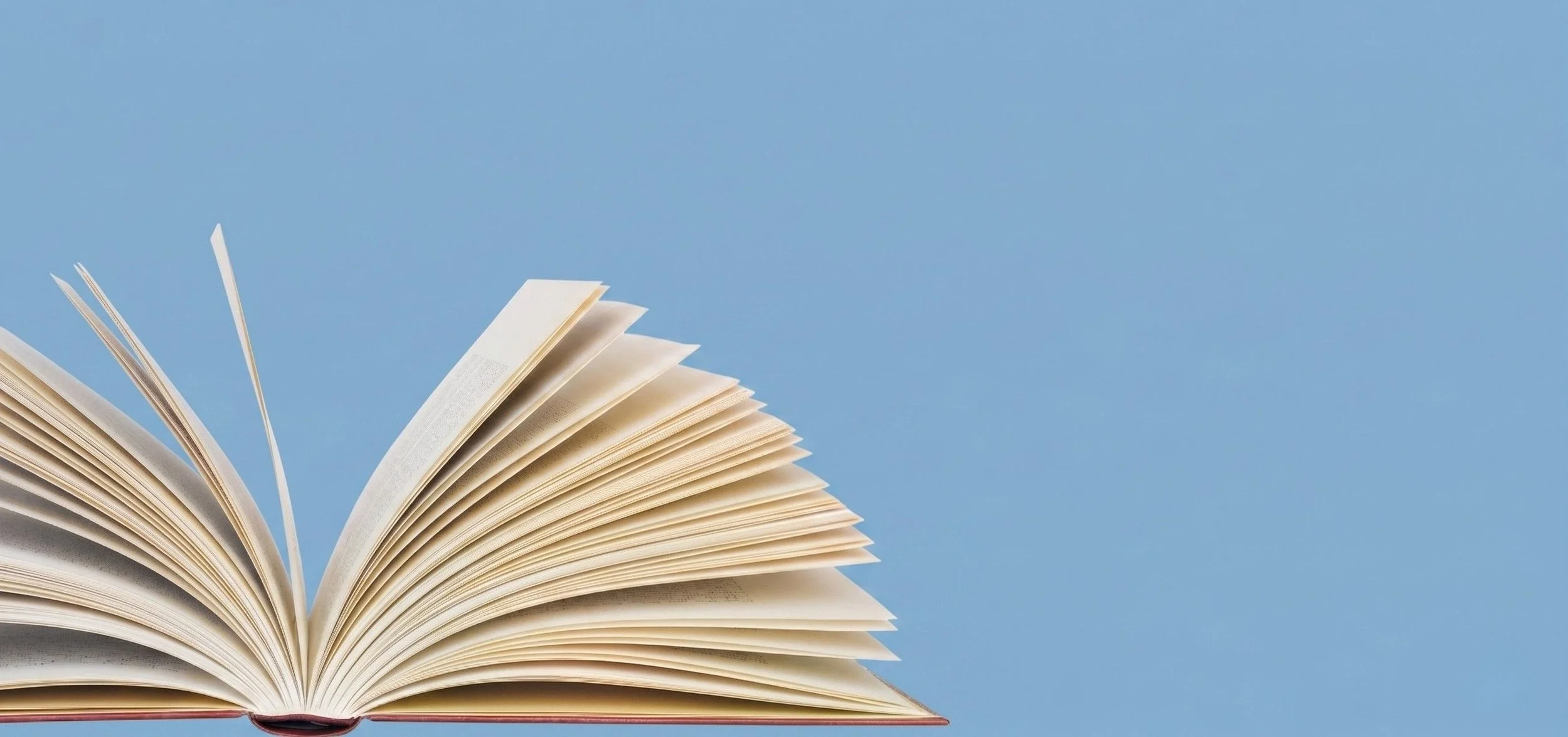 An open book with pages fanned out against a clear blue sky background.