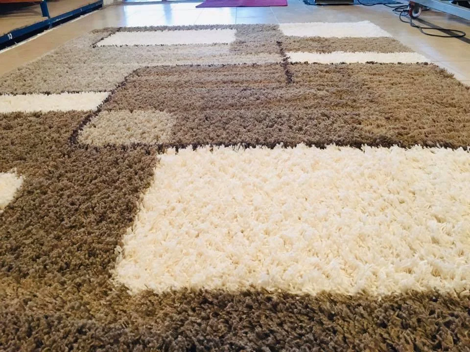 Close-up of a geometric-patterned shaggy rug with sections of various shades of brown and white in a room.