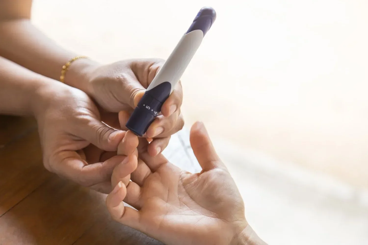 Hands holding a blood sugar test device to a fingertip, preparing for a prick.