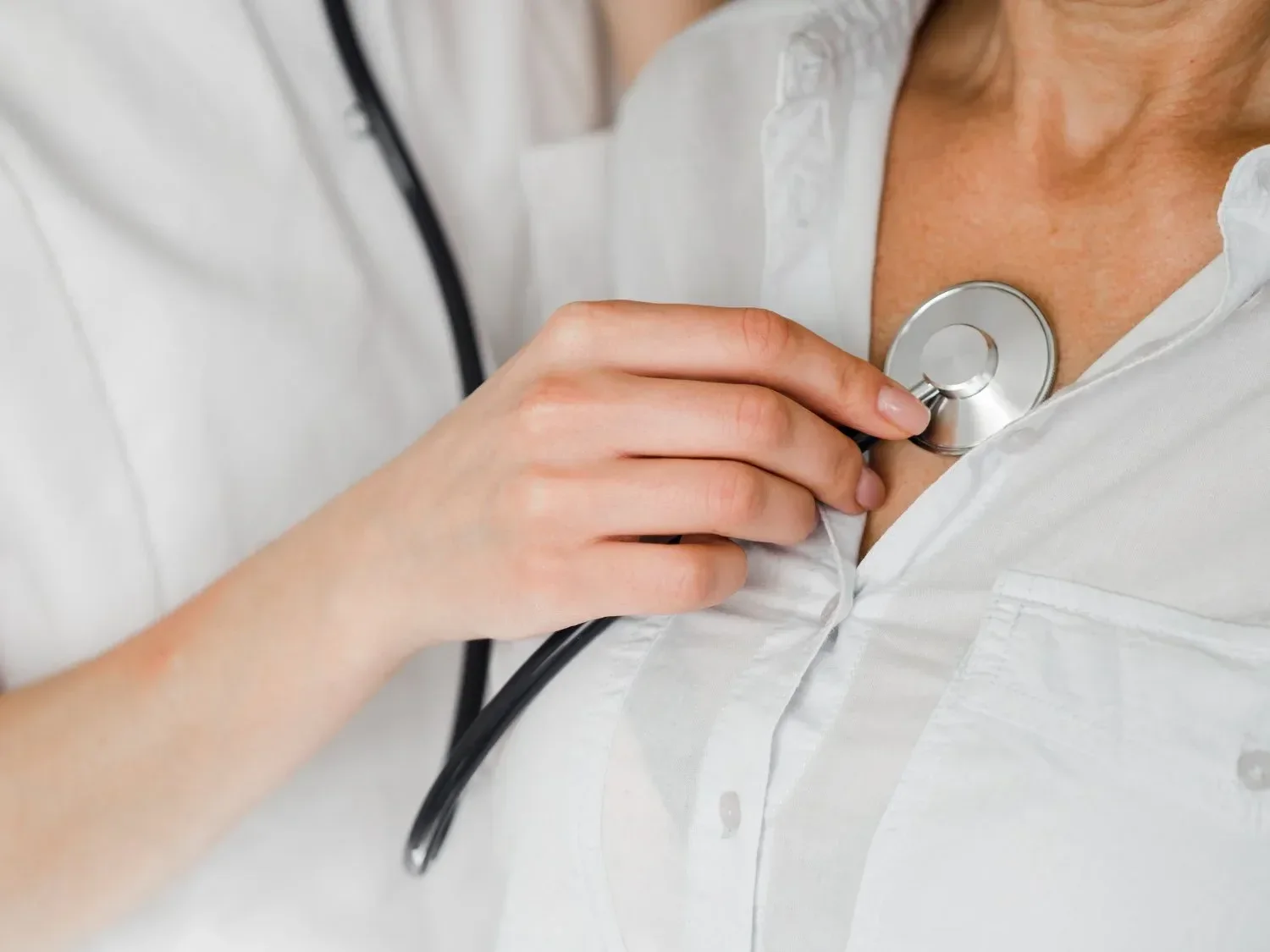 A healthcare professional uses a stethoscope on a patient's chest, both in white attire, conveying a clinical and caring atmosphere.