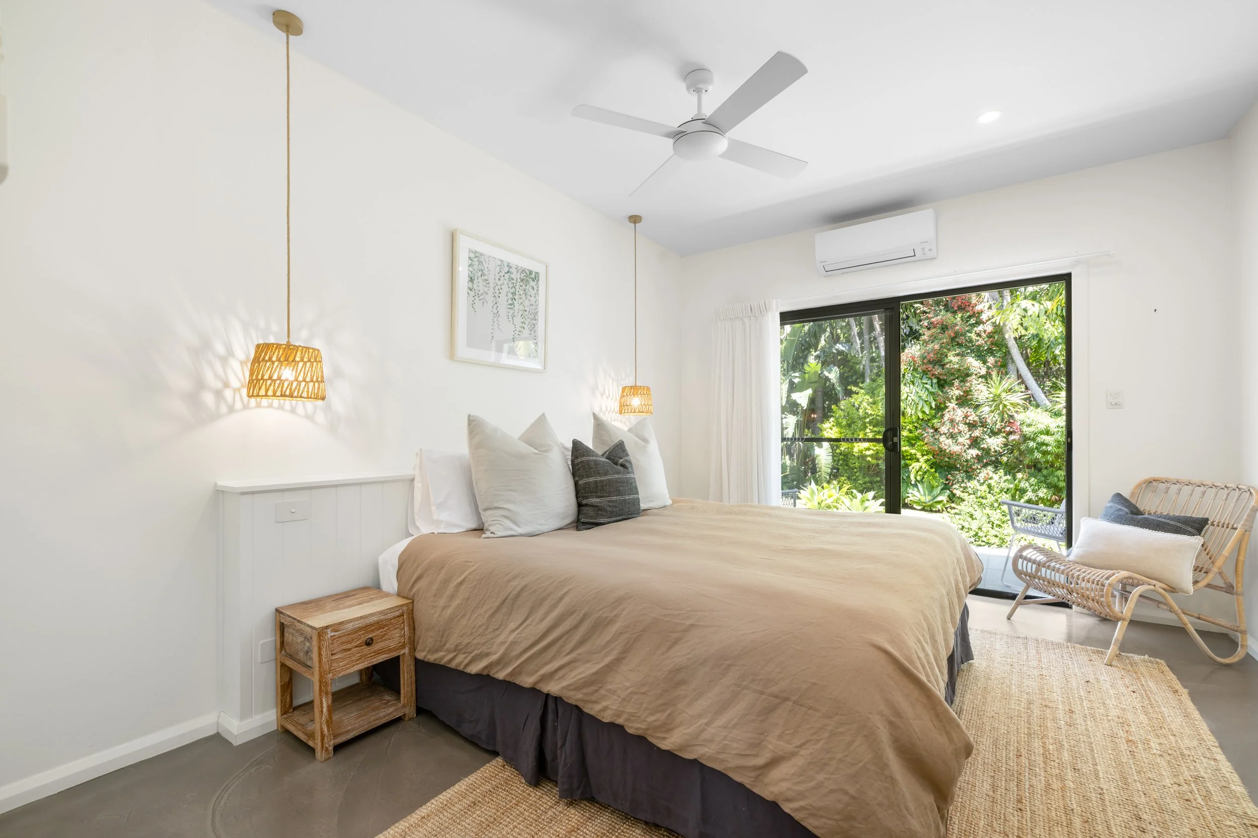 A spacious, modern living room with white sofas, a round wooden coffee table, a large window with sliding doors, and an open kitchen area with white cabinets and a marble backsplash.