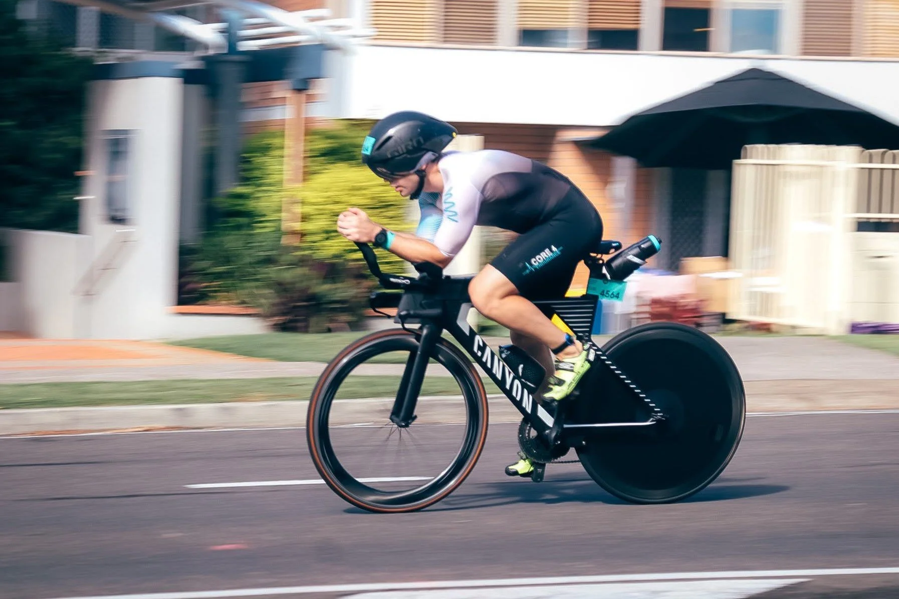A person riding a racing bike on a street, wearing a helmet, black and white cycling attire, and neon green shoes.