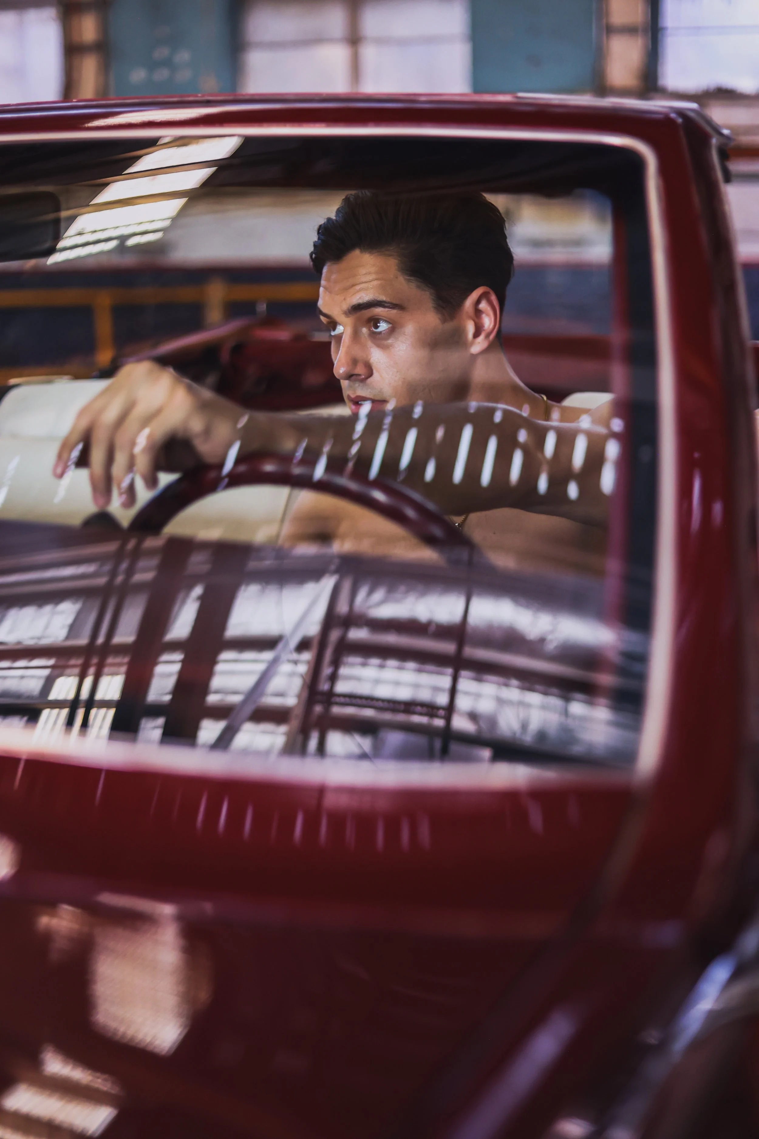 Kelvin Van Vuuren is sitting inside a vintage red car, looking through the windshield with a pensive expression. Athlete photoshoot.