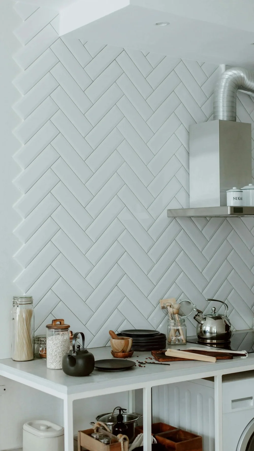 White herringbone tile backsplash beside a kitchen range hood