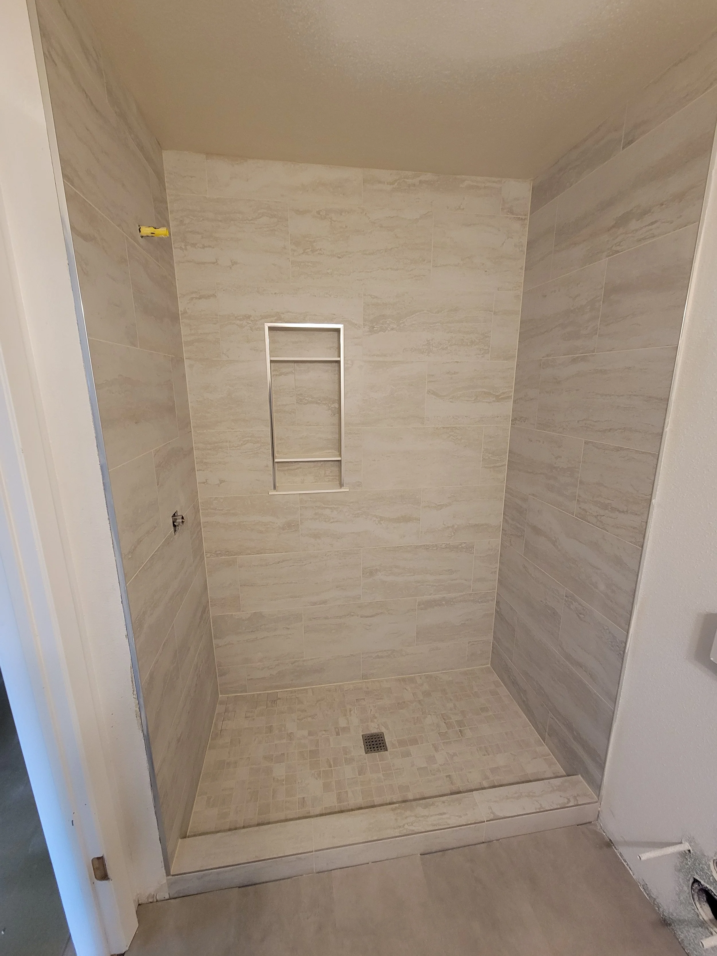 Empty shower with beige tile walls, a built-in niche, and a drain on the floor.