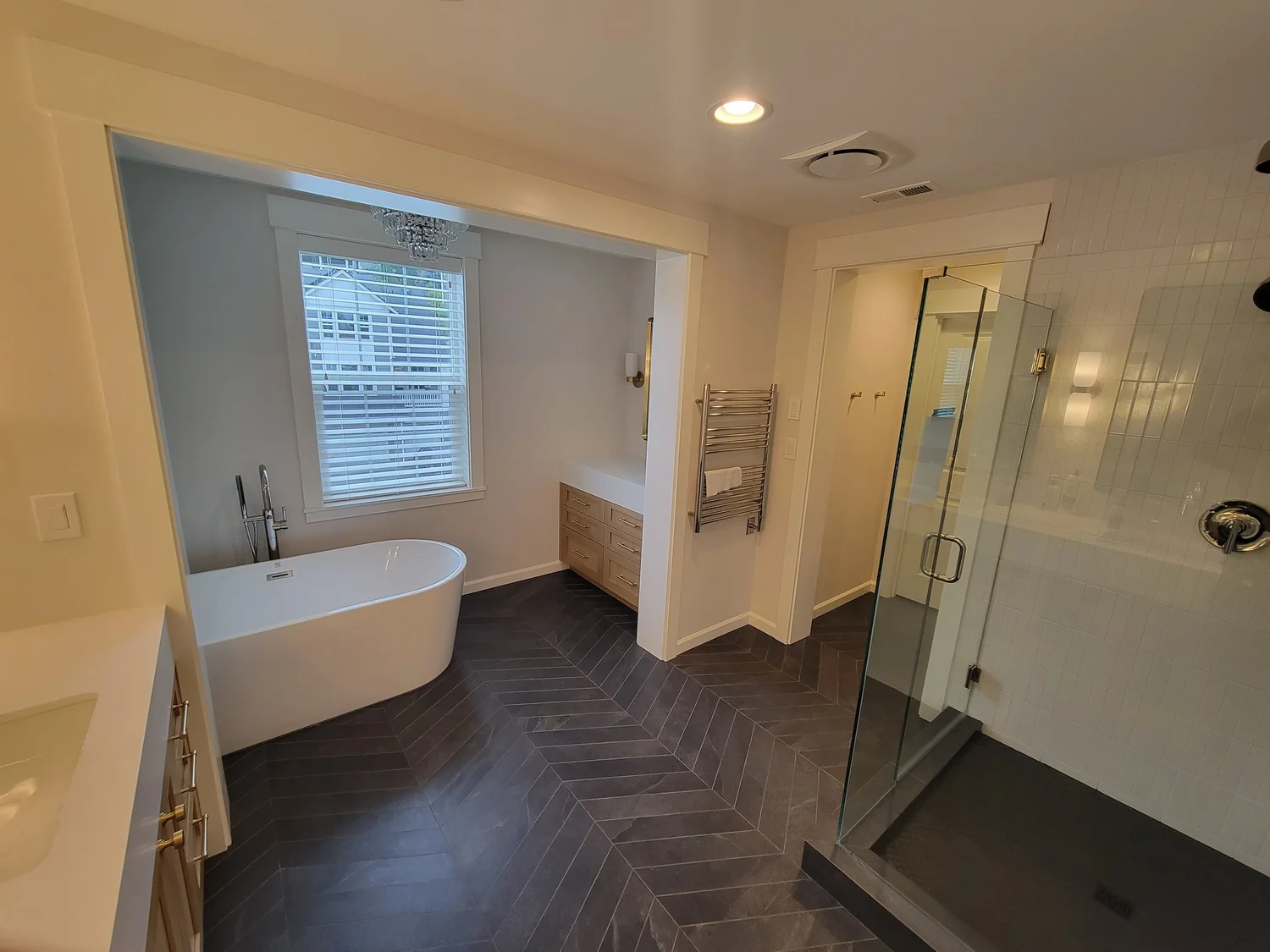 Dark herringbone tile flooring in a bathroom with a bathtub, glass shower and wood vanity