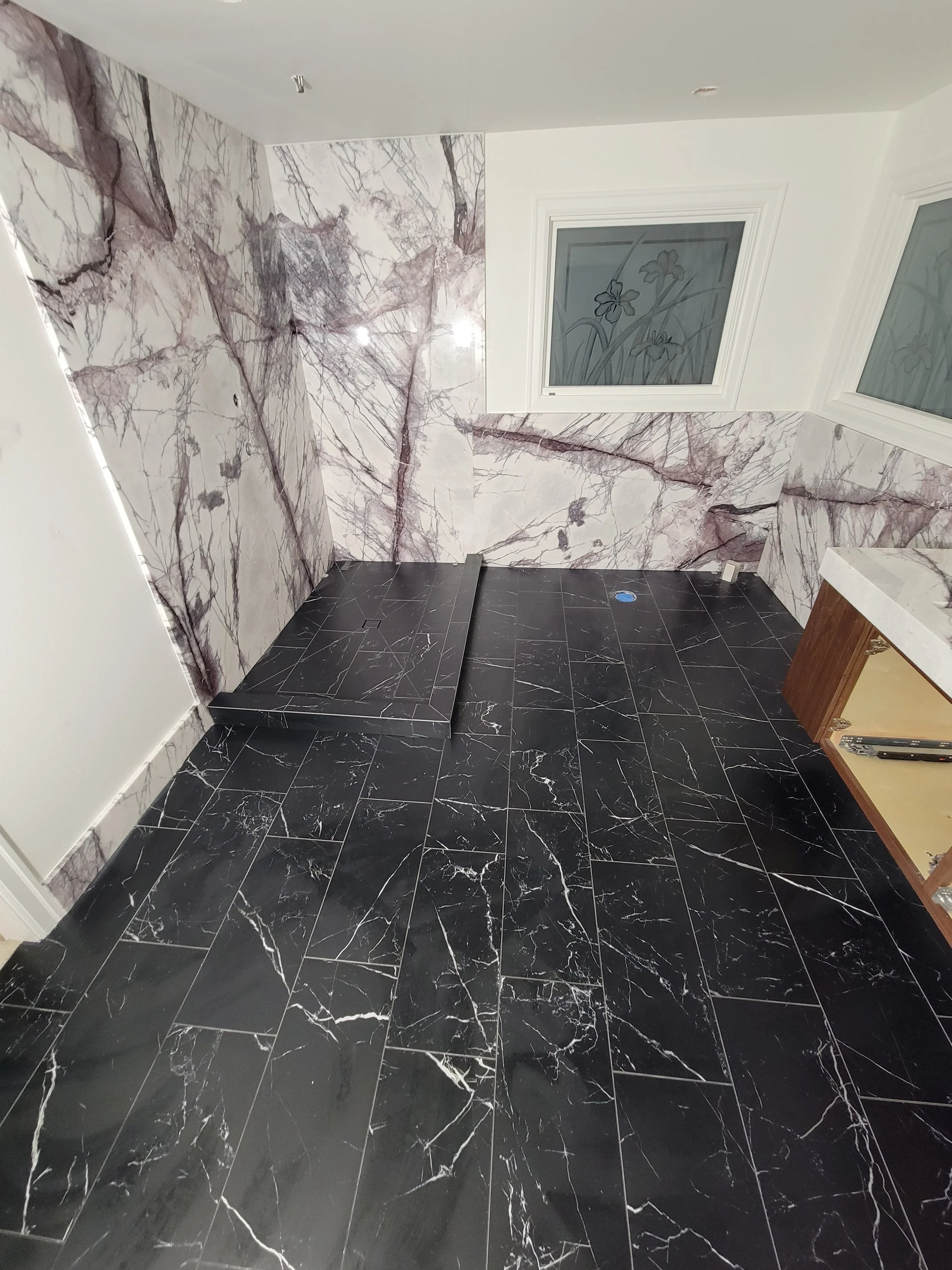 Room with black marble floor and purple veined marble walls, two windows with floral etched glass, and a small shower or wet area in the corner.