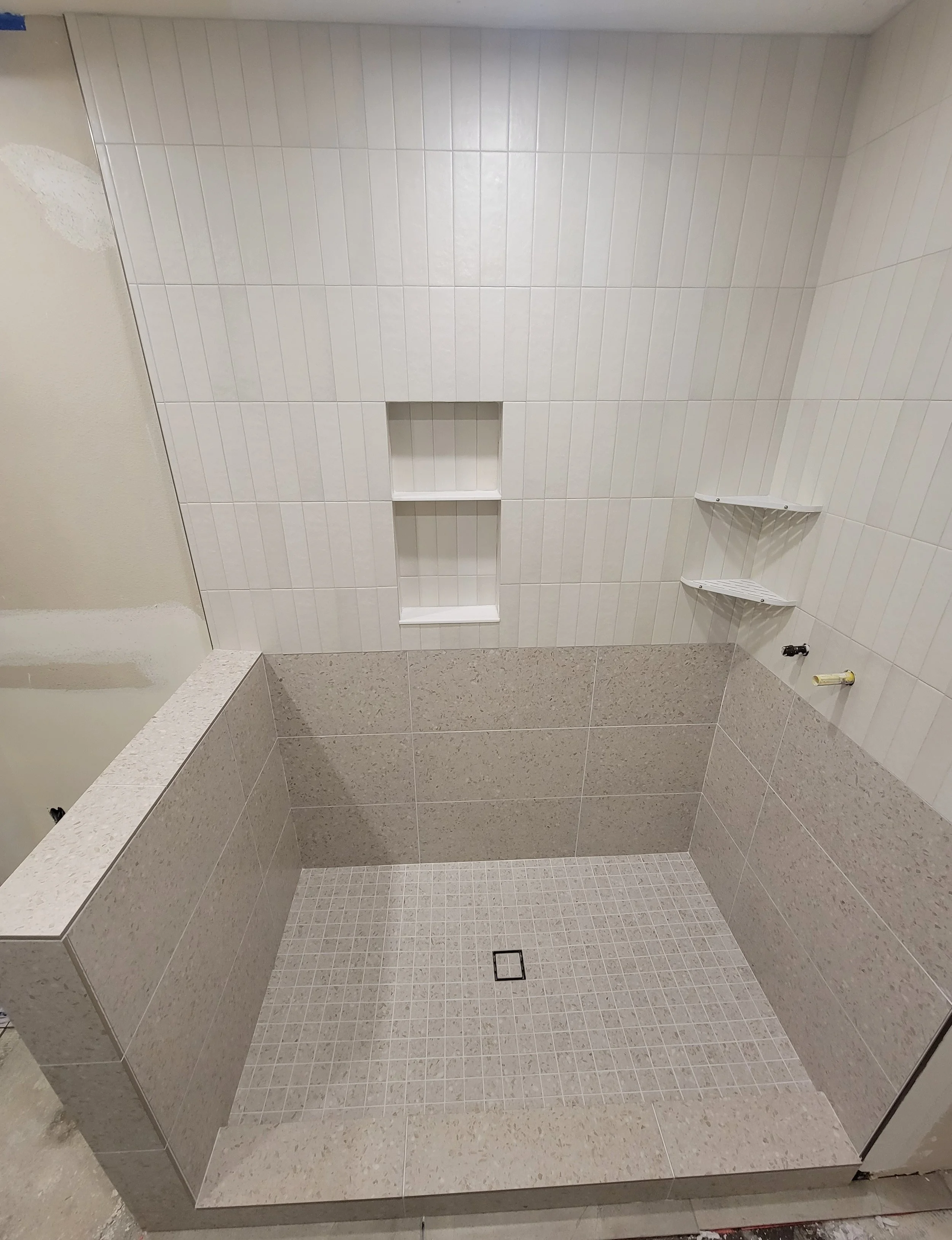 Shower area with beige and white tiled walls and floor, built-in niche, and corner shelves.