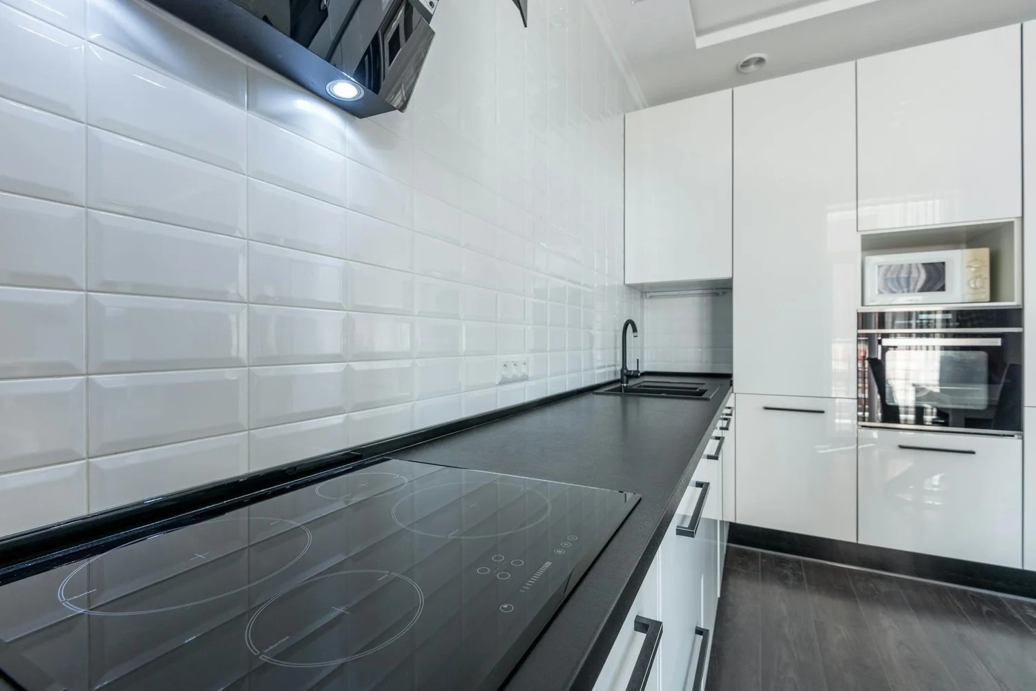 White subway tile kitchen backsplash above a dark countertop beside a sink and white cabinets