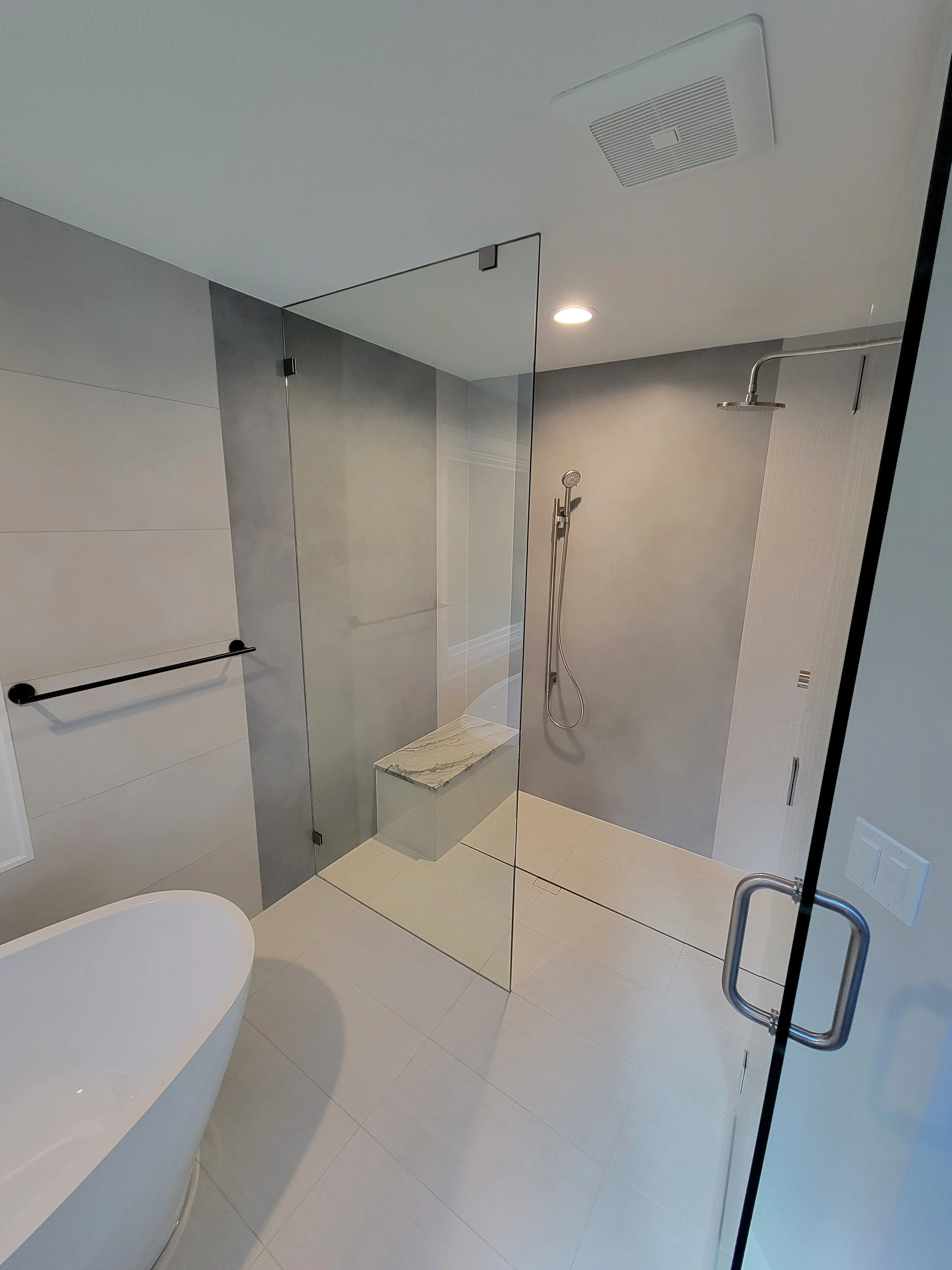 Modern bathroom with walk-in shower enclosed by glass, featuring a mounted showerhead and a built-in seat with marble top, next to a bathtub and black towel bar.