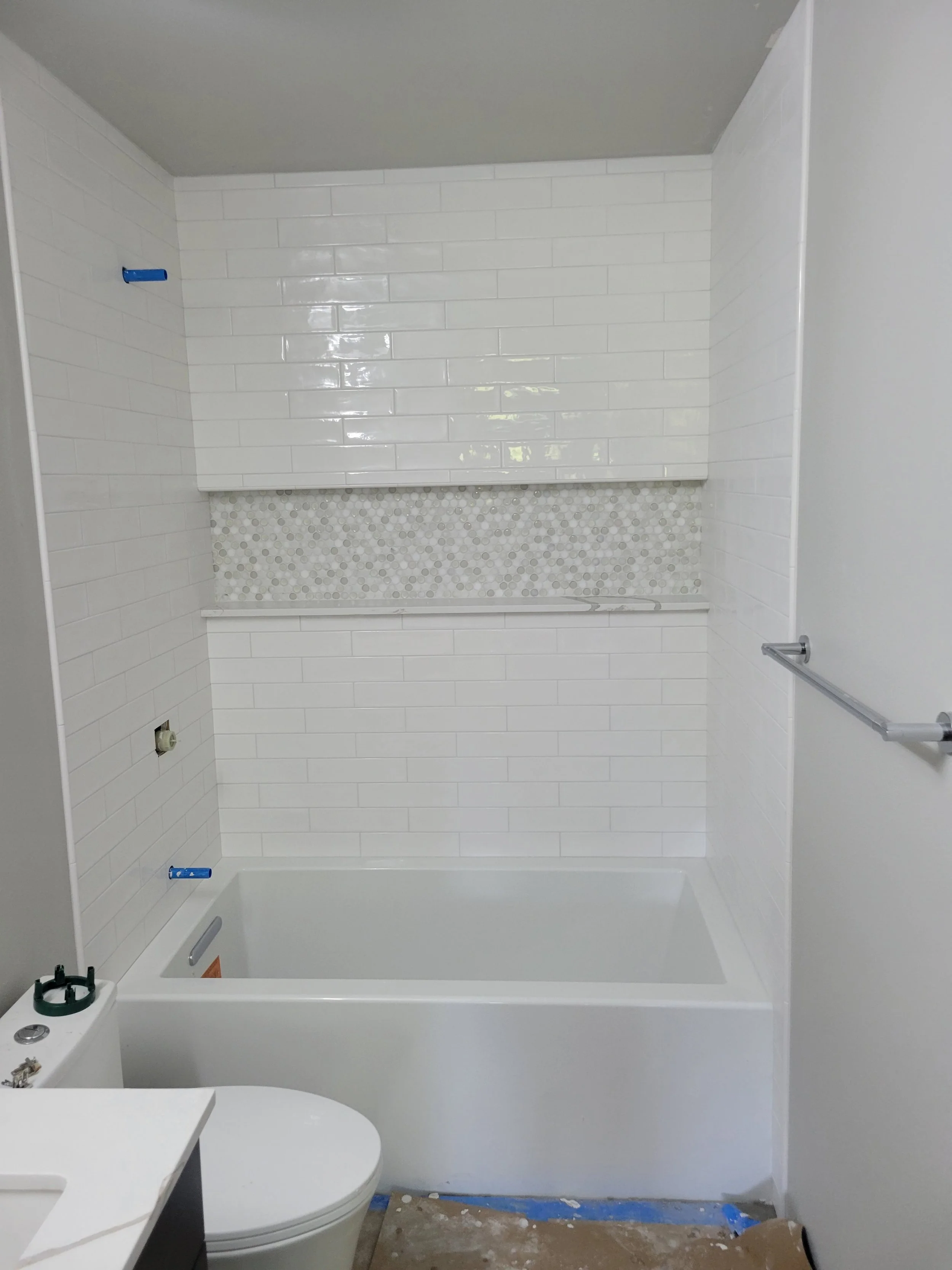 Bathroom with white subway tile walls, a bathtub, partial view of a toilet, and construction materials and tools nearby.