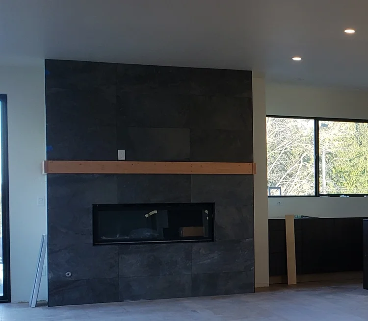 Dark tiled fireplace surround with a horizontal wood mantel