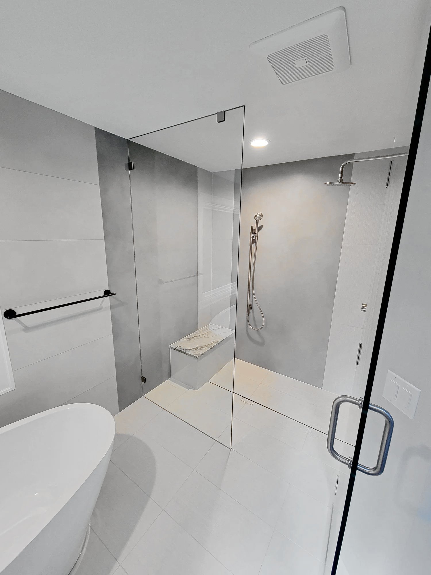 Walk-in tile shower with glass enclosure, a built-in bench and large-format wall tile