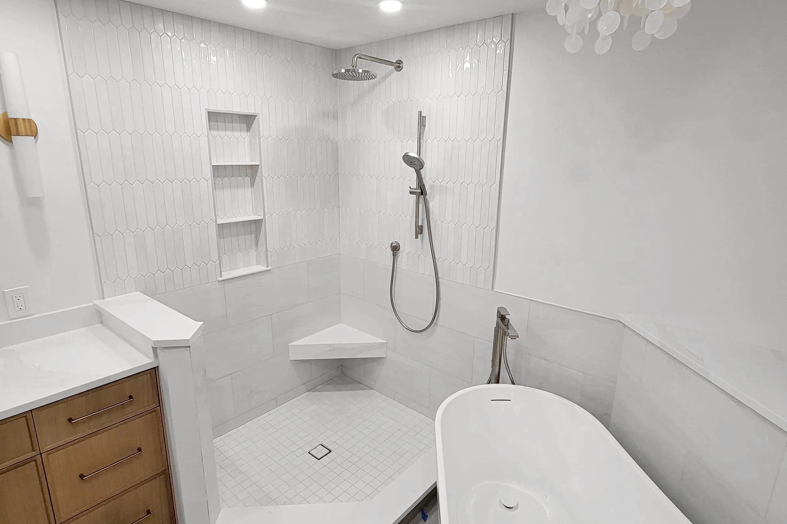 Custom tiled shower with a recessed niche, corner bench and freestanding bathtub