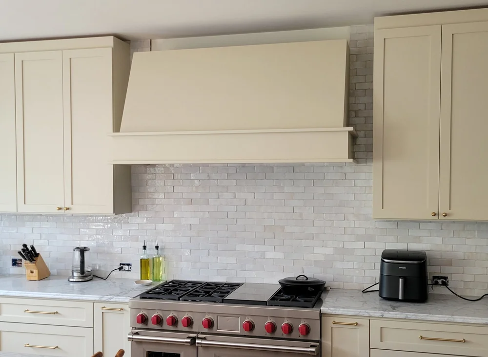 White subway tile backsplash behind a range beneath a paneled kitchen hood