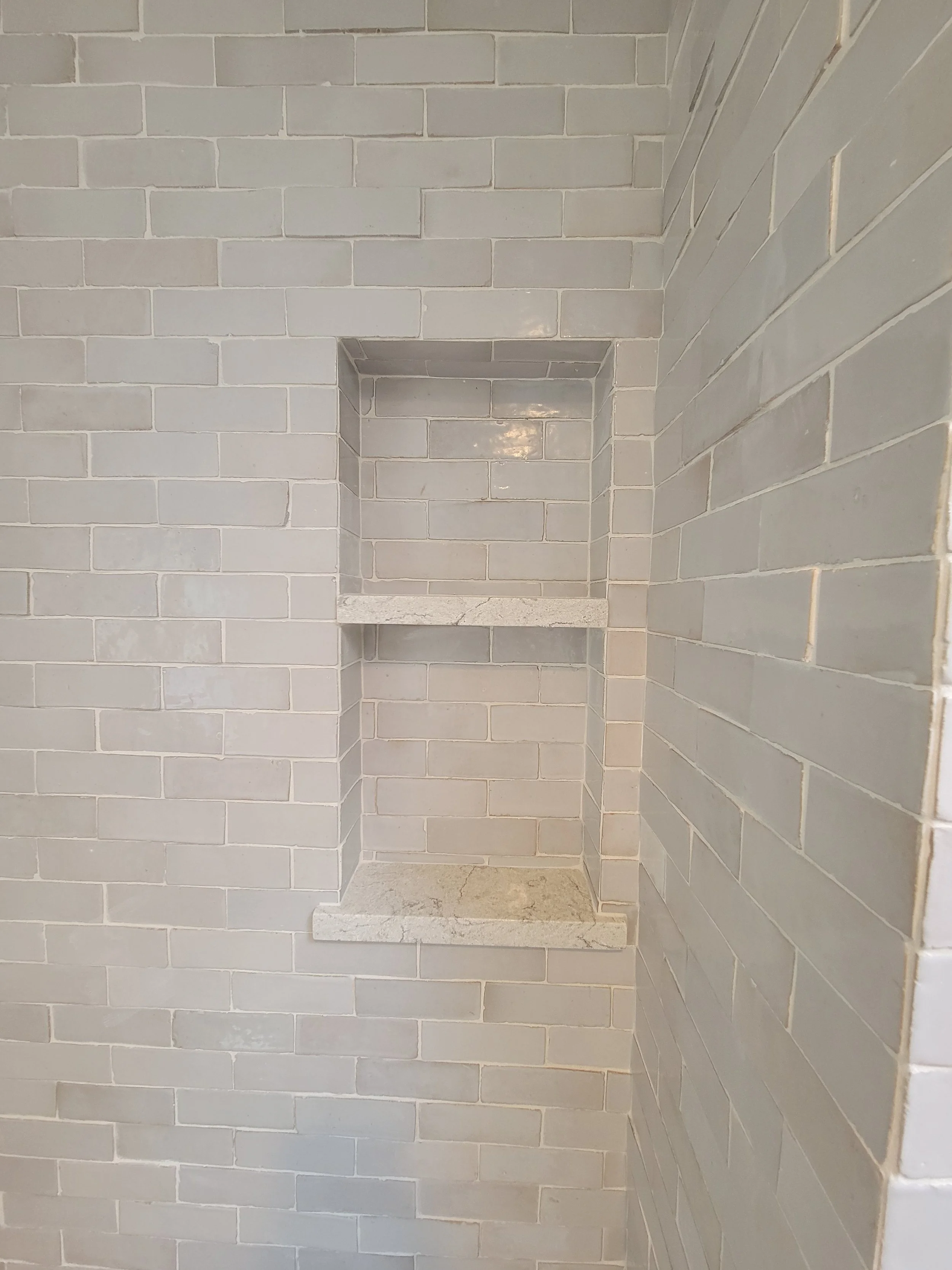 A built-in corner shower niche with two shelves, tiled with beige subway tiles.