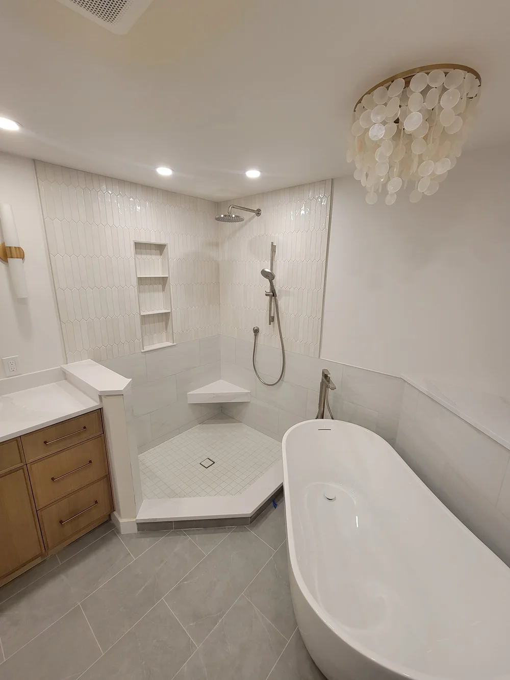 Completed tile shower with recessed shelves, corner bench, glass enclosure and freestanding tub