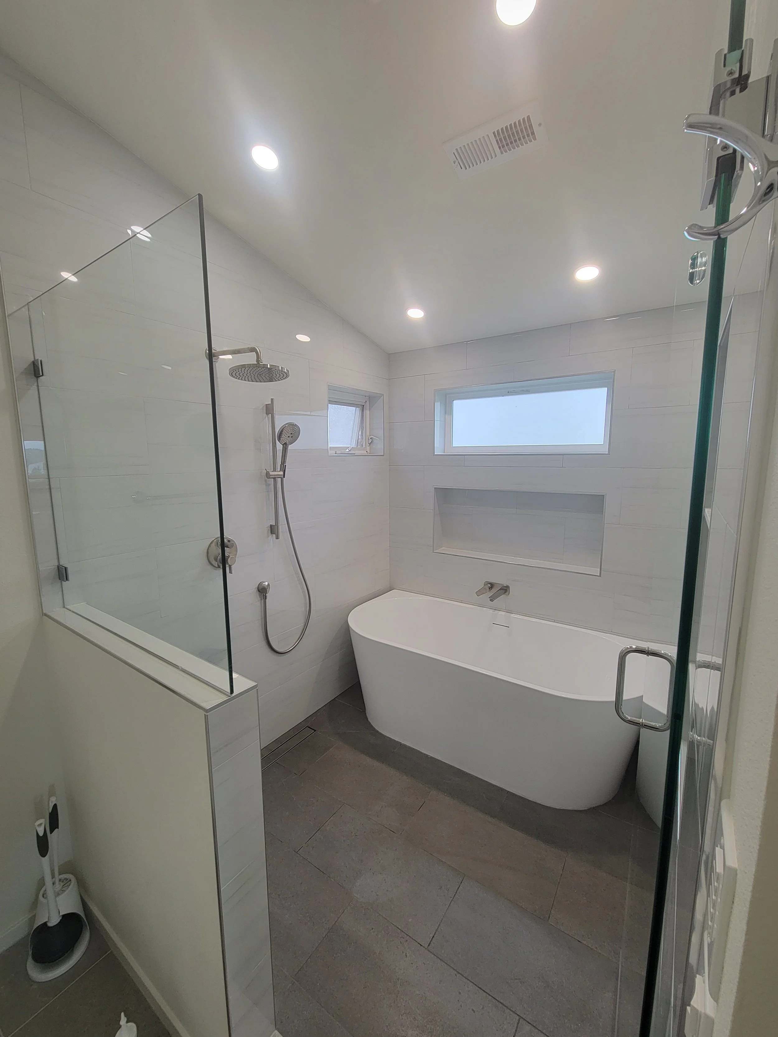 Modern bathroom with a bathtub, glass-enclosed shower area with a rain shower head, small horizontal window, and recessed ceiling lights.