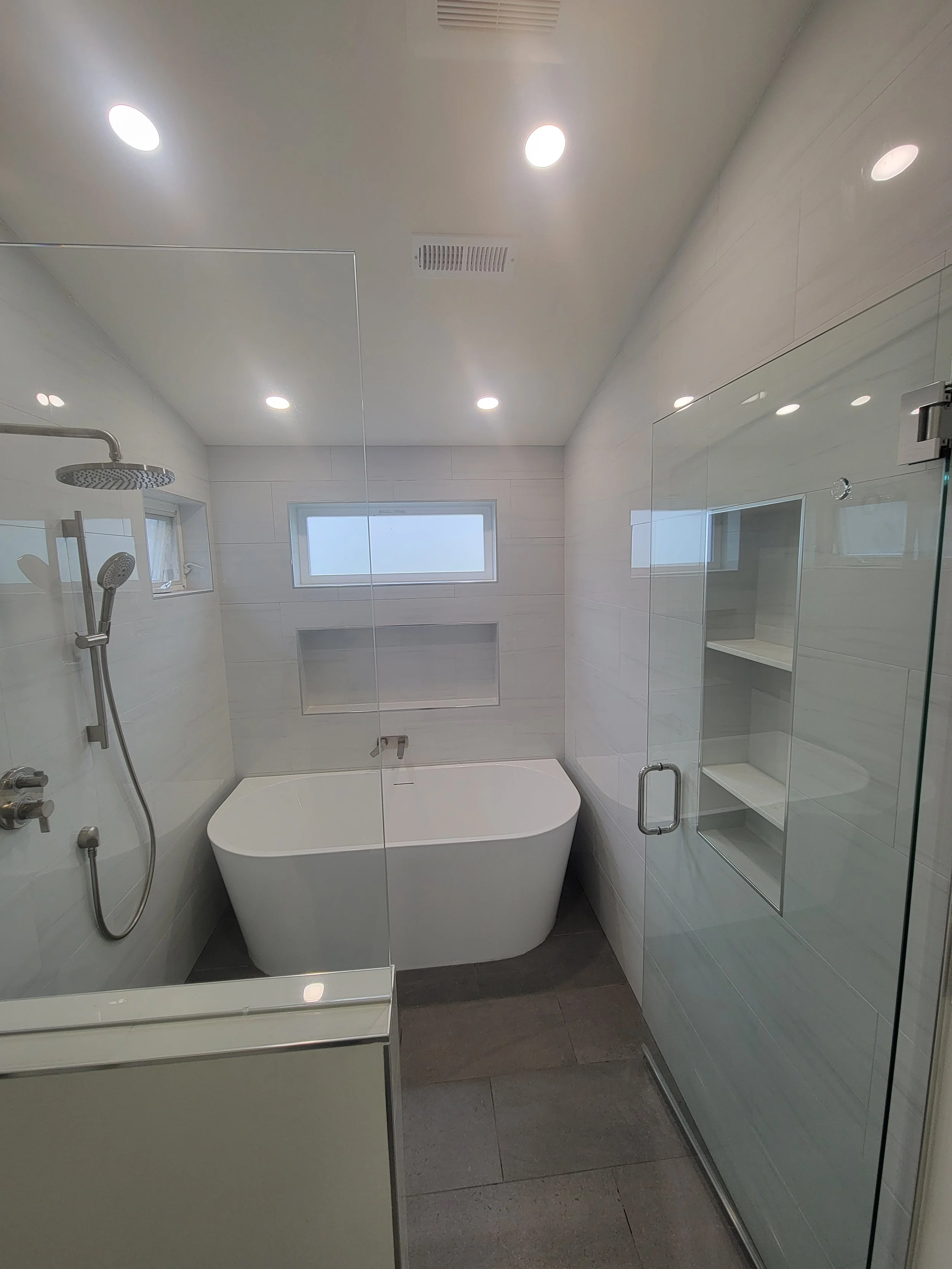 Modern bathroom with white walls, a freestanding bathtub, a glass shower enclosure, and small horizontal windows near the ceiling.