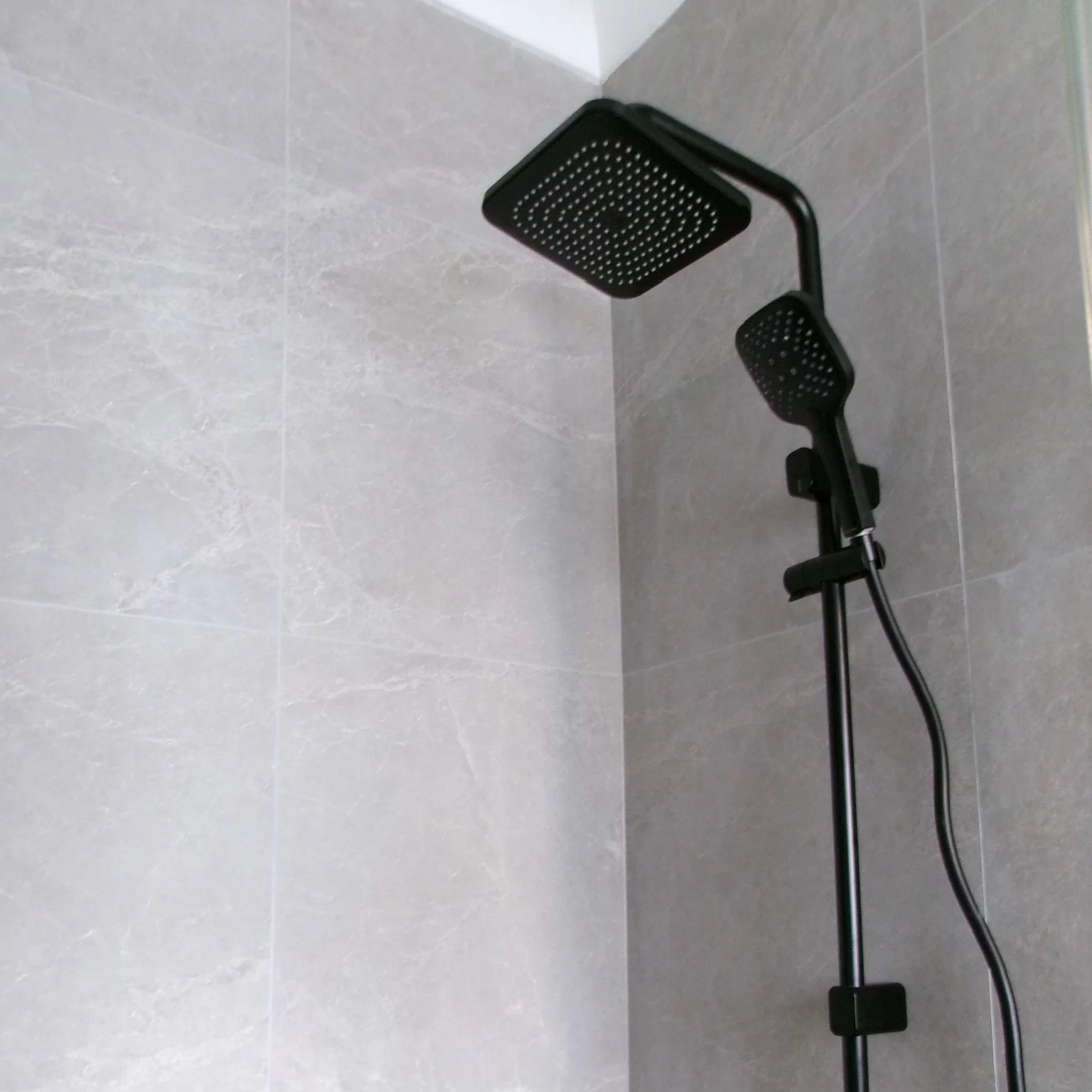 A black modern showerhead with a handheld attachment mounted on a gray tiled wall.