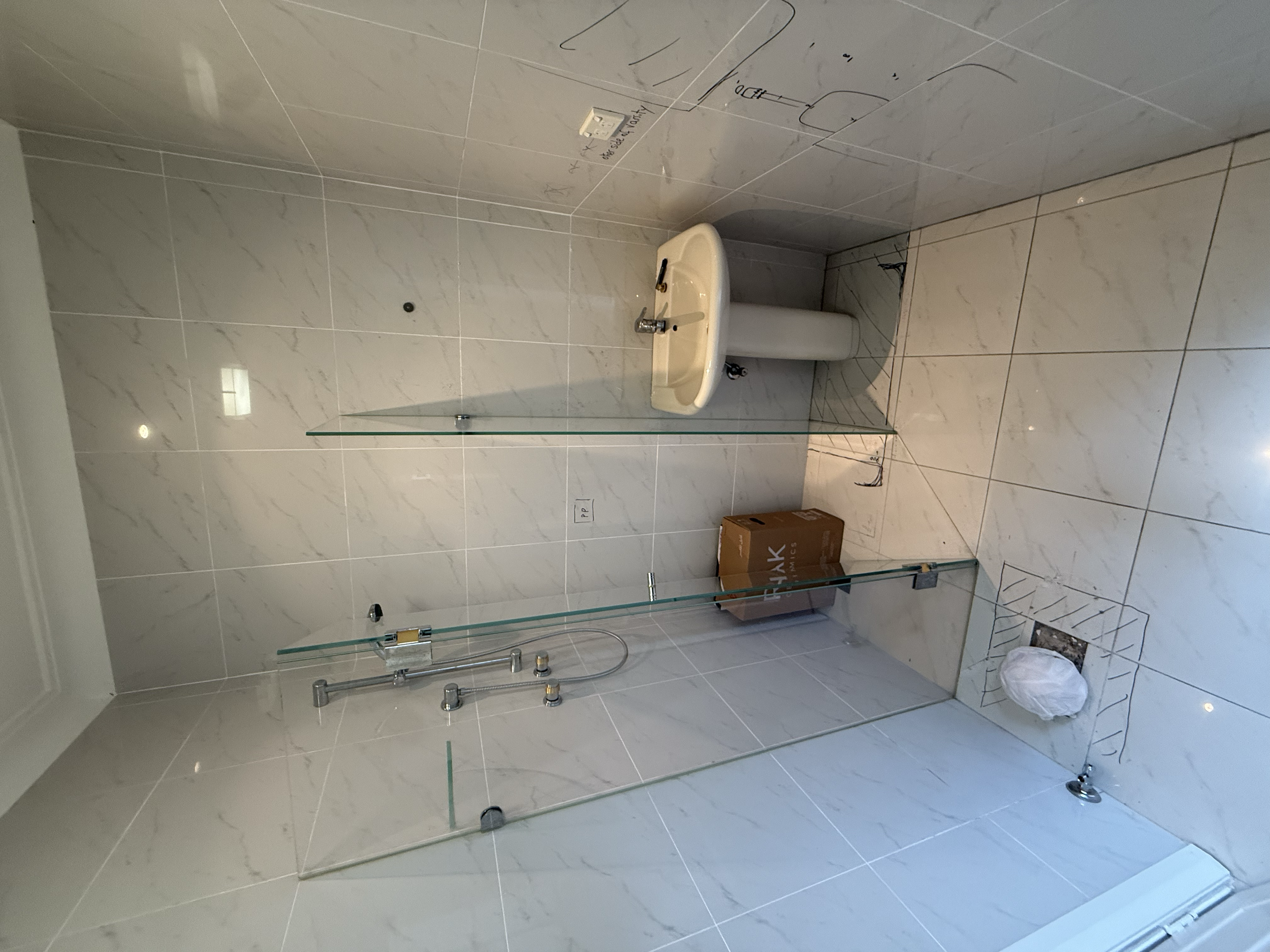 Bathroom with a tiled shower area, a white pedestal sink, and a cardboard box on the floor. The shower has glass panels and a showerhead.