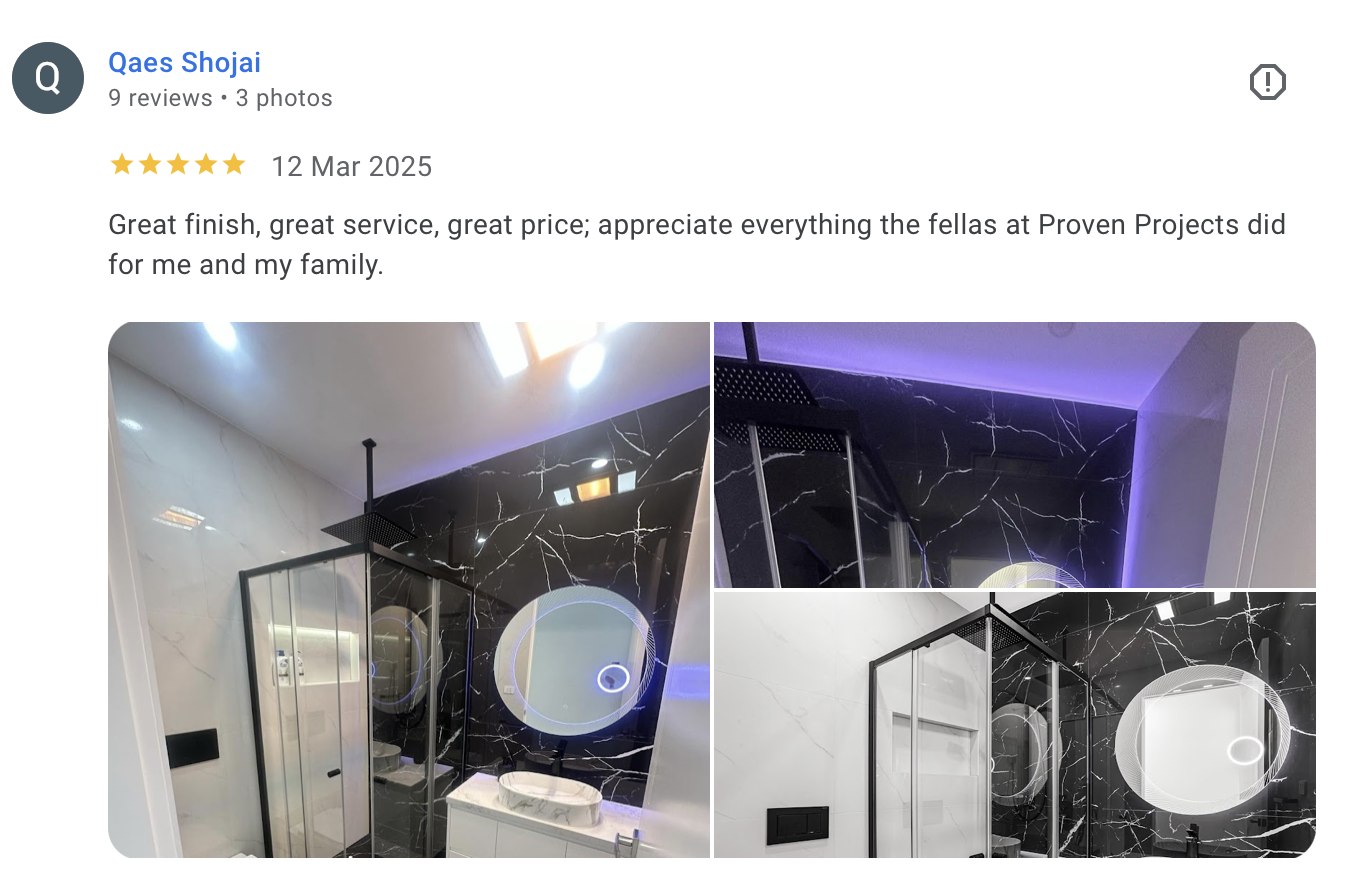 Modern bathroom with black marble walls, a rain showerhead, a backlit round mirror, and a white vanity with a vessel sink.