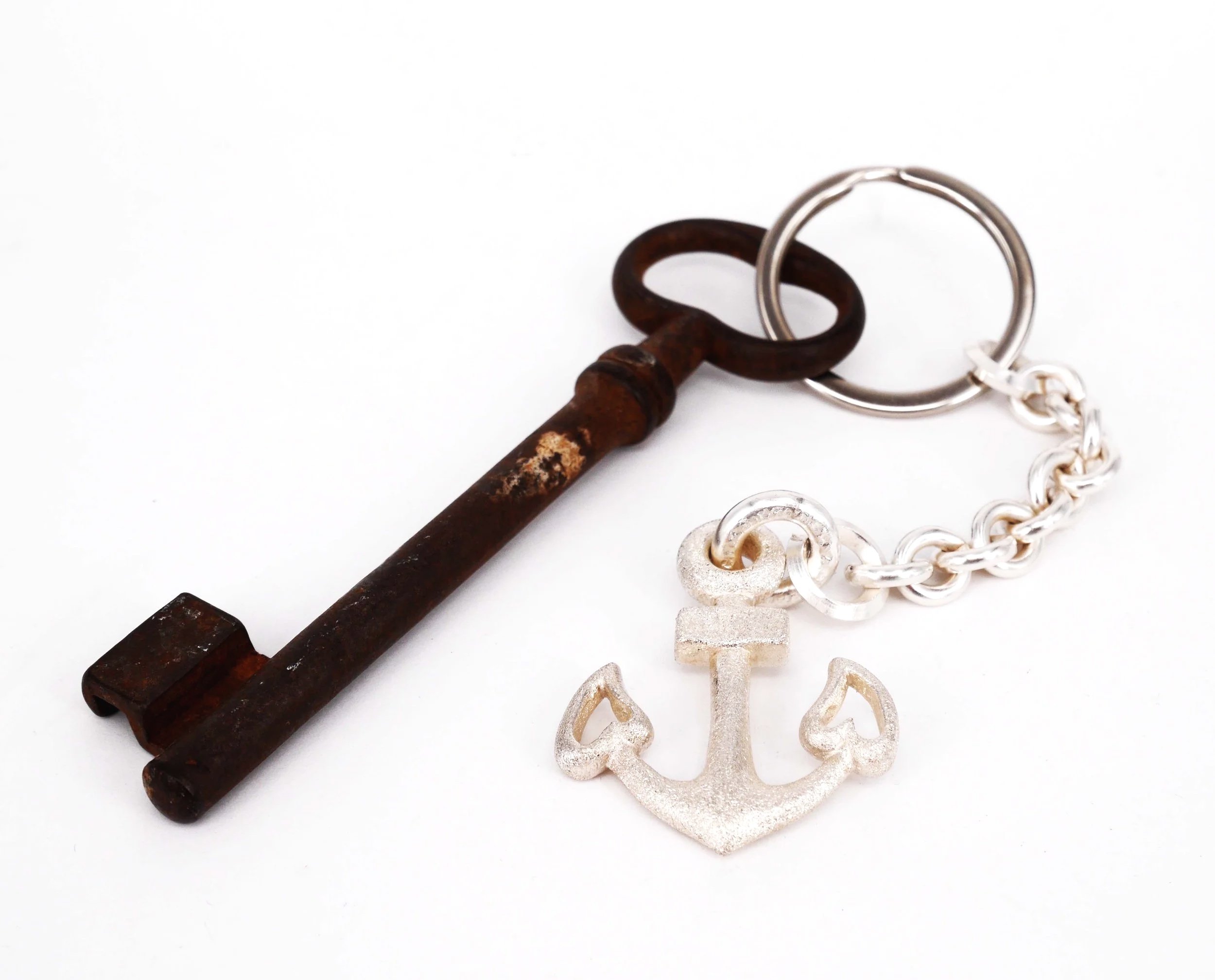 Ein alter, rostiger Schlüssel mit einem Schlüsselring, verbunden mit einer silbernen Kette mit einem Ankeranhänger.