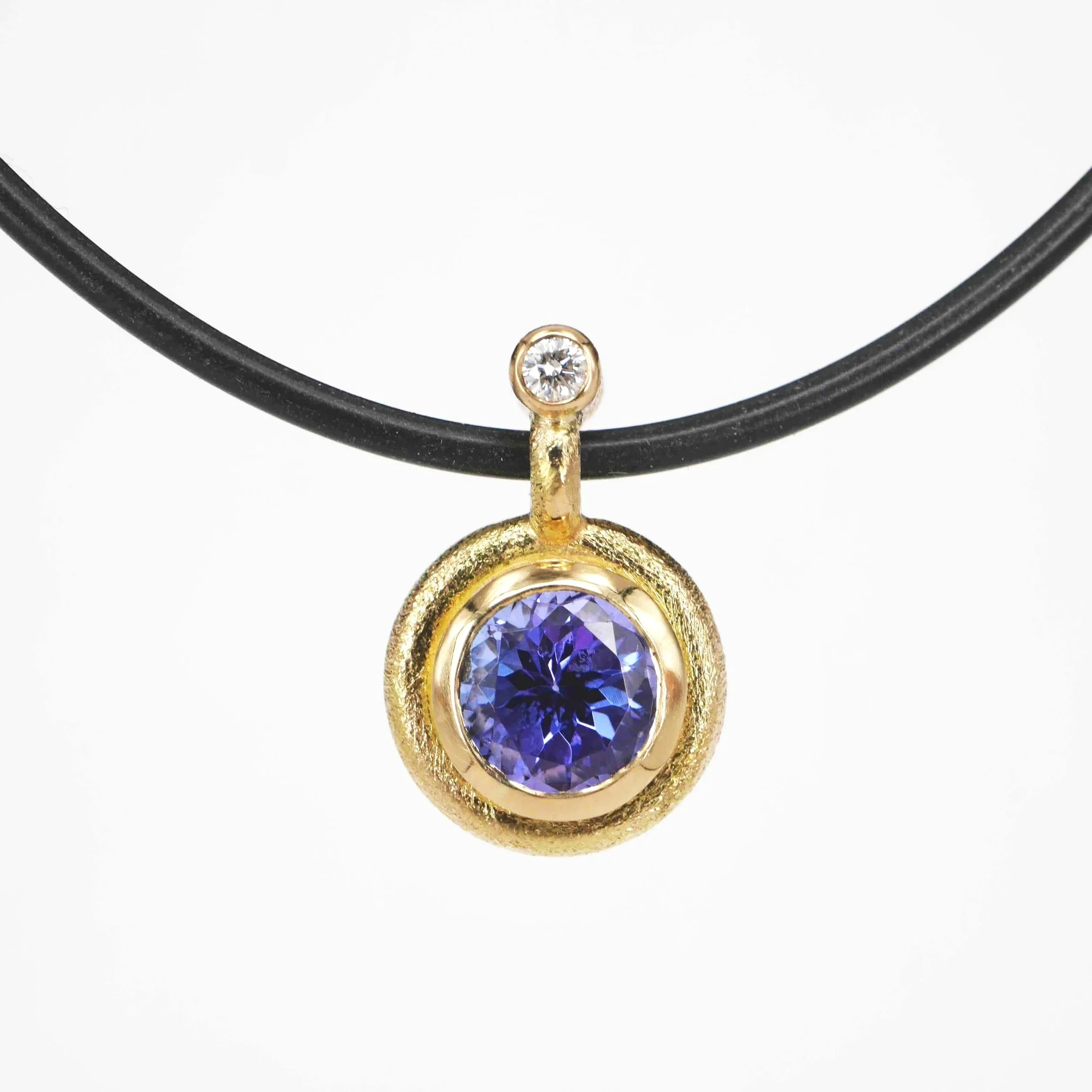 Ein goldener Anhänger mit einem großen blauen Edelstein und einem kleinen weißen Edelstein, aufgehängt an einem schwarzen Band