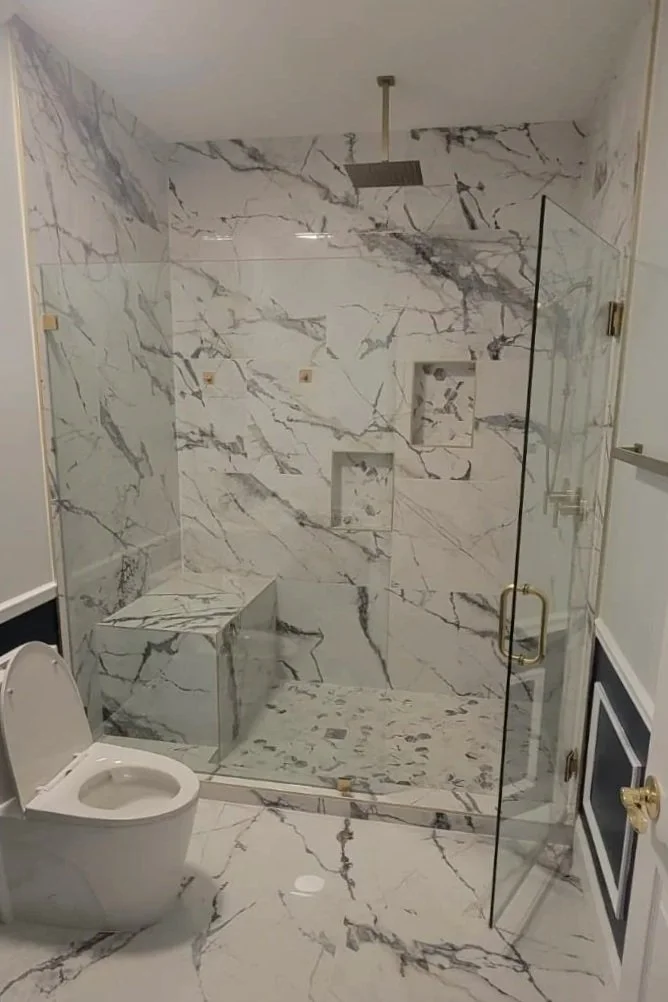A bathroom with a marble tile shower, a glass door, and a white toilet.